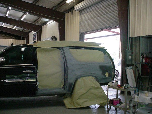 SUV in a body shop, masked for paint; tan paper covers the sides.