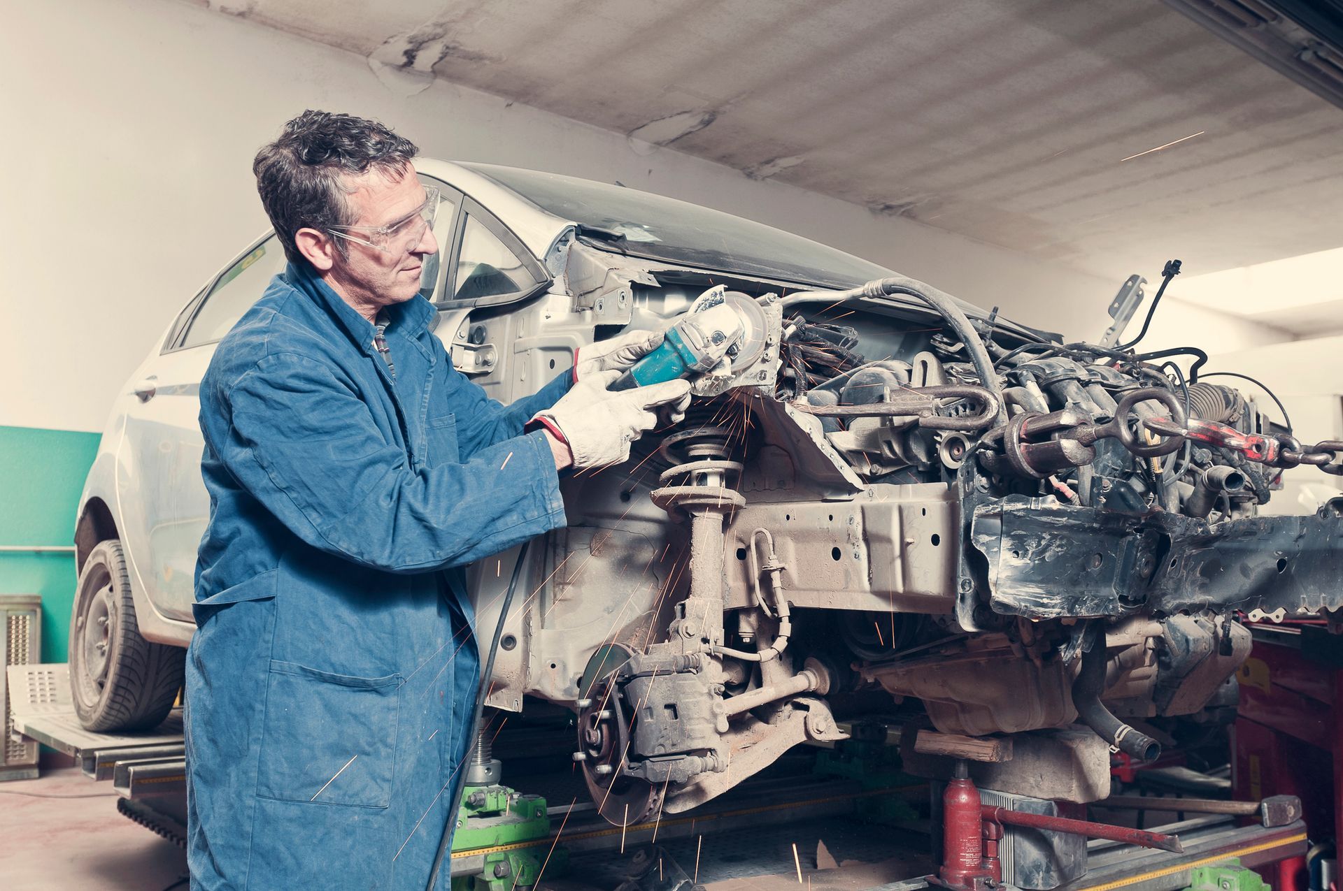 A mechanic in a garage, engaged in auto collision repair, surrounded by tools and car parts. A mechanic in a garage, engaged in auto collision repair, surrounded by tools and car parts.