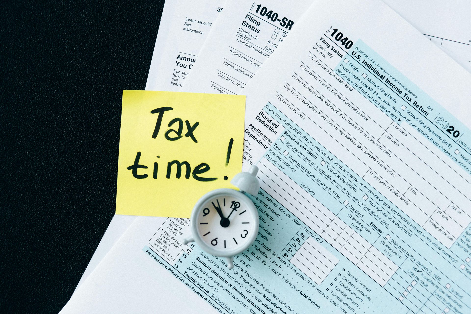 A clock sits on top of a tax form next to a sticky note that says tax time