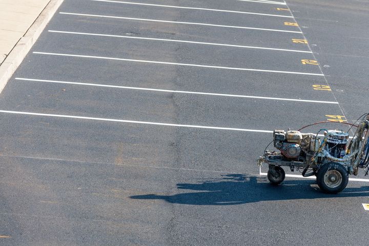 A machine is painting white lines on a parking lot.