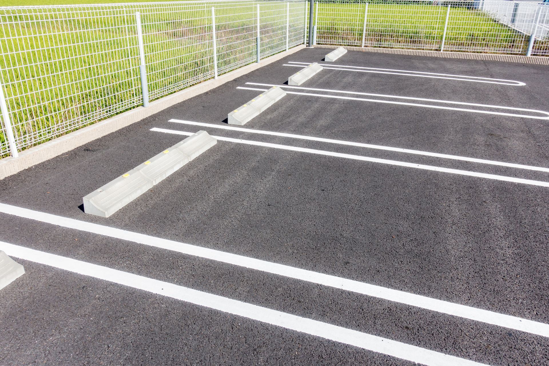A parking lot with white lines and a fence in the background.