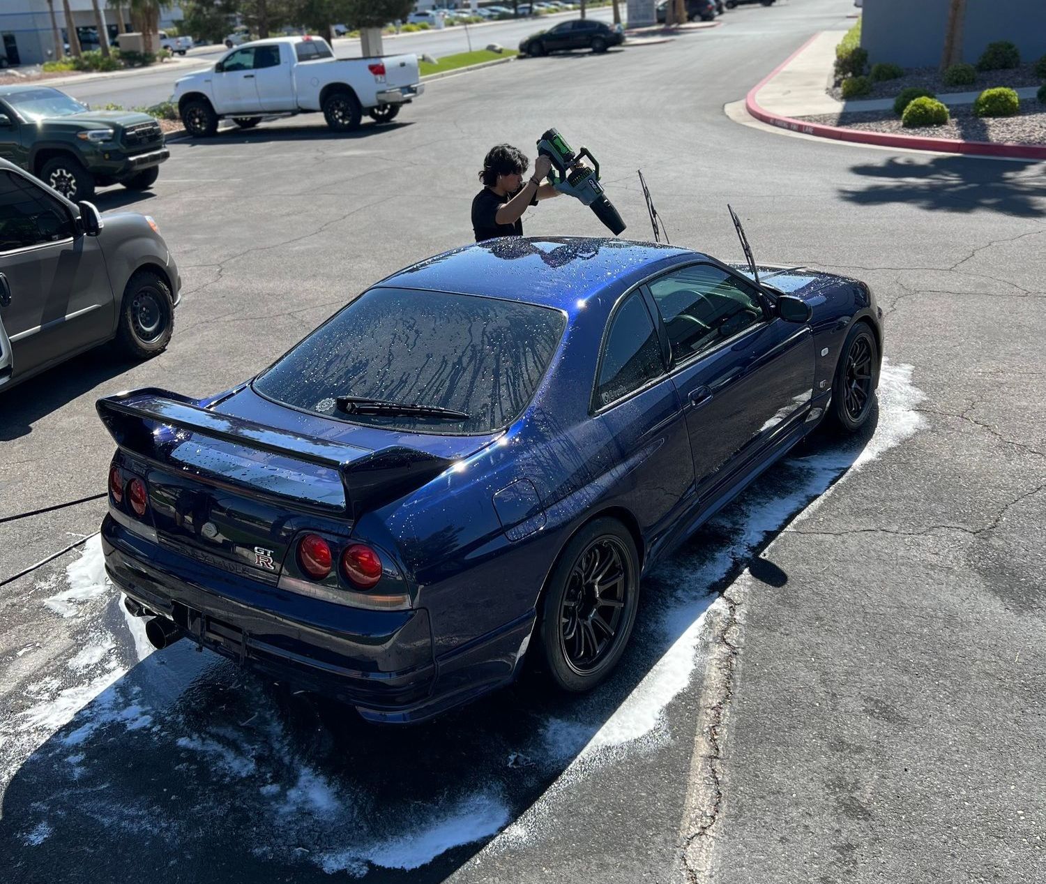 A man is washing a blue car in a parking lot