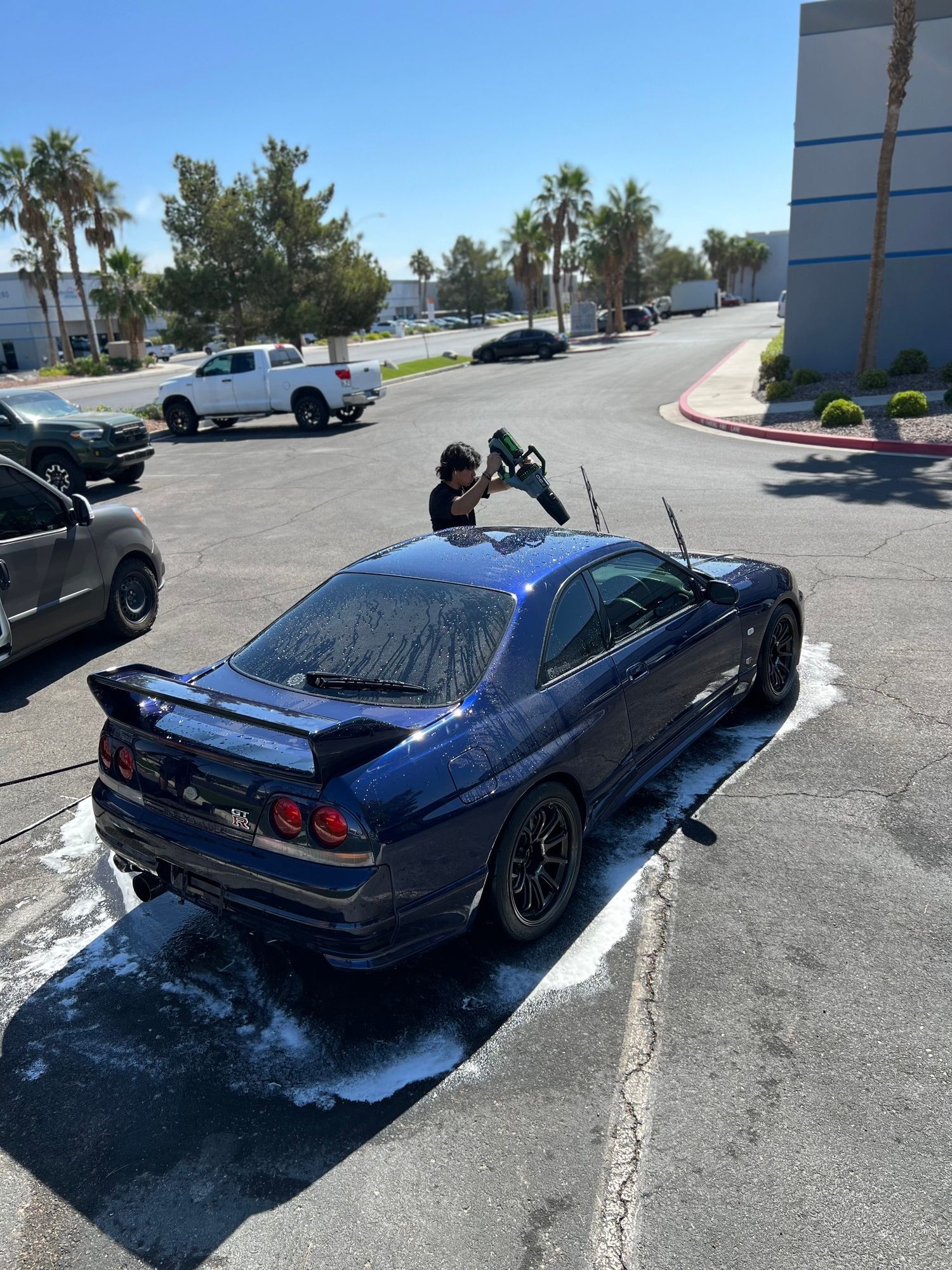 A man is washing a blue car in a parking lot