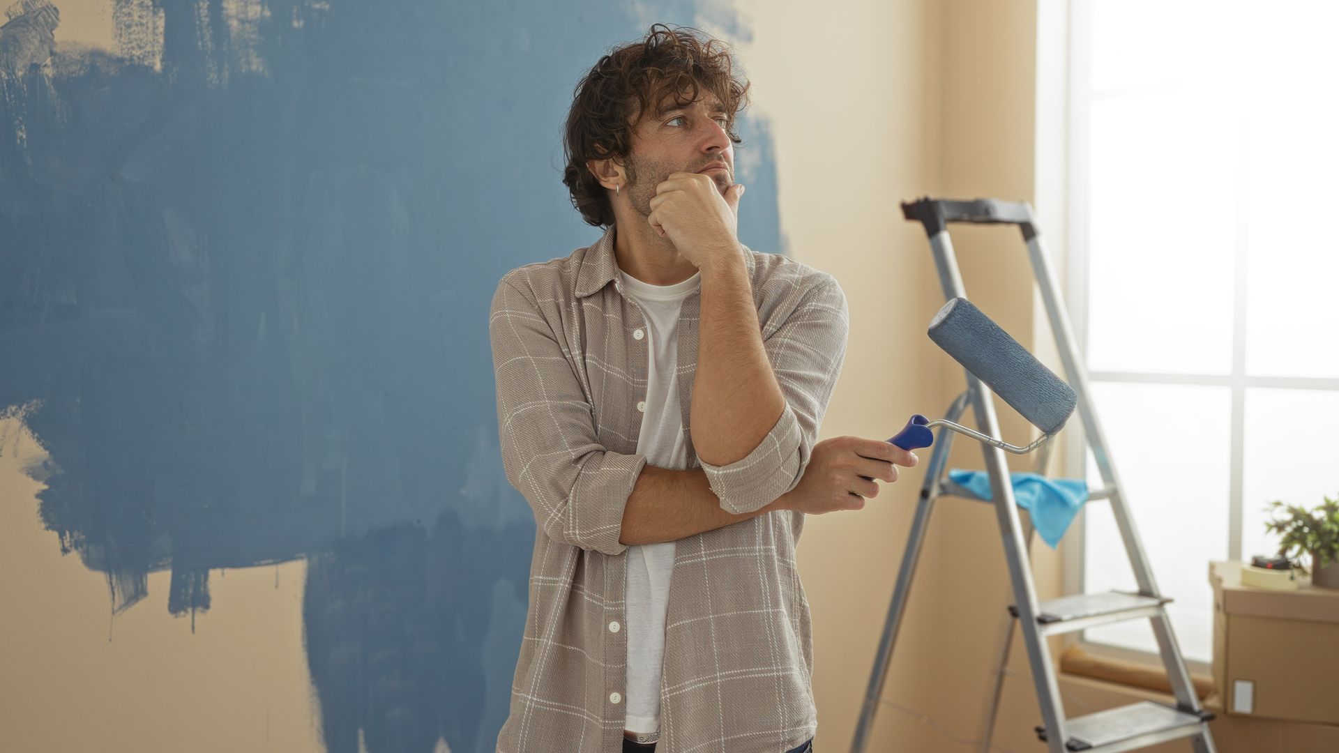 A man is standing in front of a blue wall holding a paint roller.