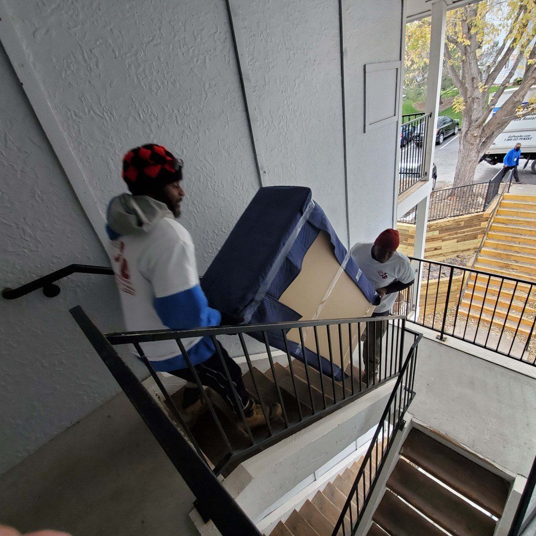 Two Men Unloading A Package In The Stairs — Aurora, CO — At Your Service Moving and Storage