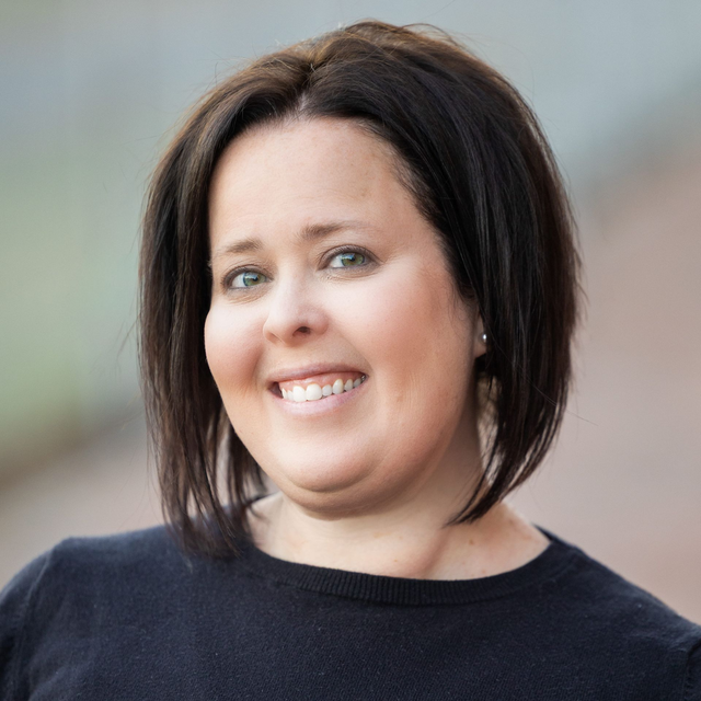 A headshot of Melissa Acosta wearing a dark shirt against a blurred outdoor background.