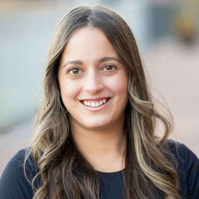 A headshot of Natalie Douglas wearing a dark shirt against a blurred outdoor background.
