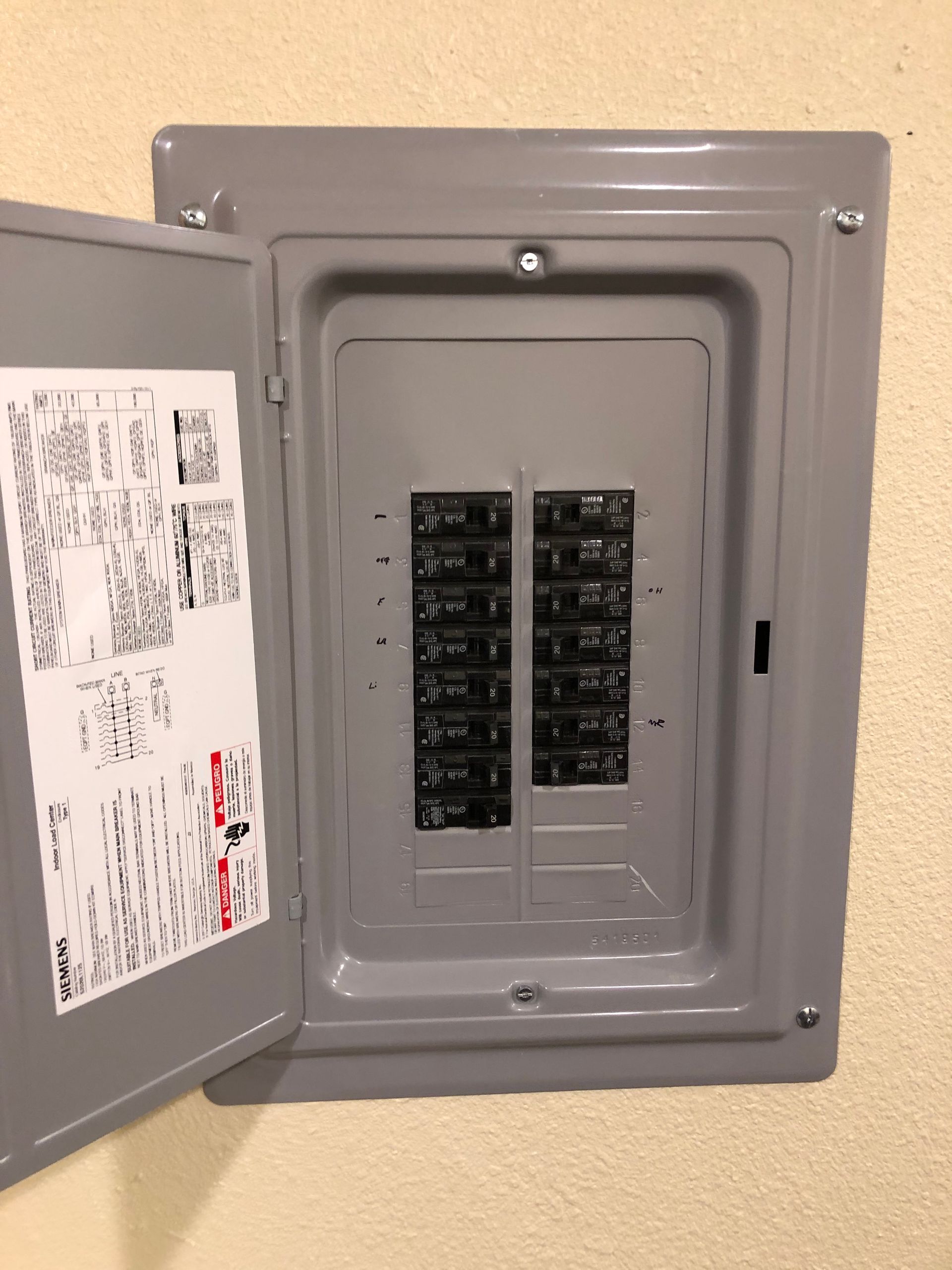 Open gray electrical breaker panel with the door open, showing rows of circuit breakers.
