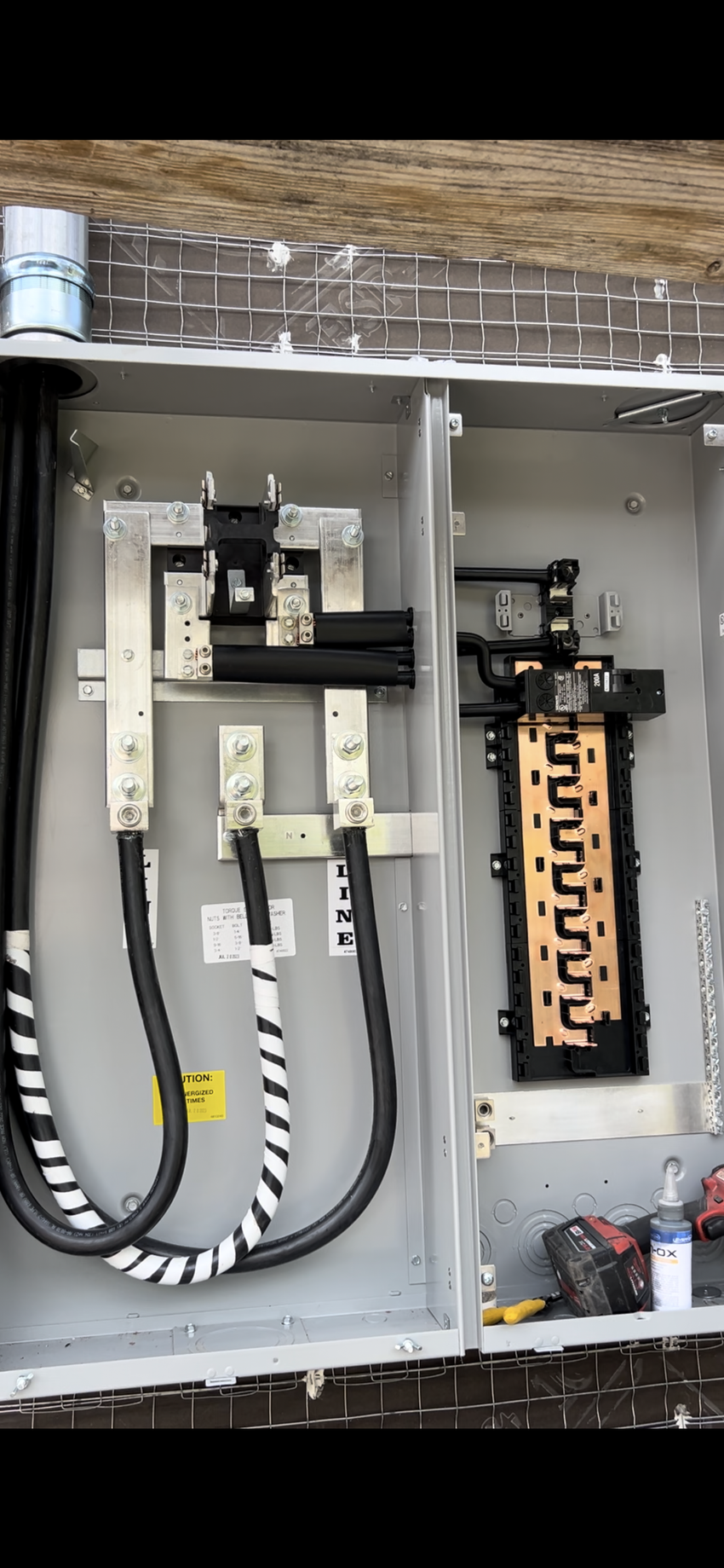 Open electrical panel with breakers, conduit, and wires mounted on a brick wall