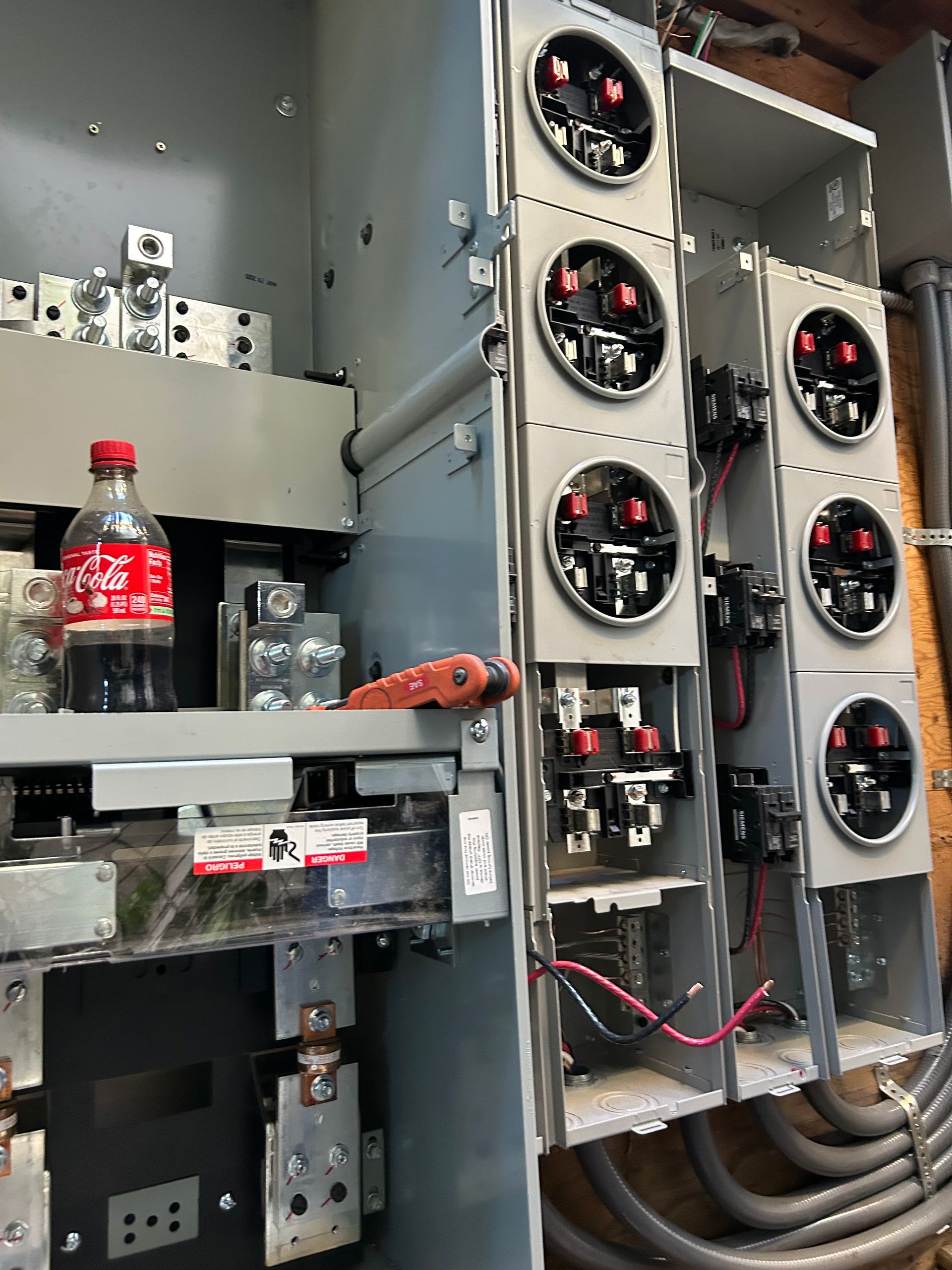 Electrical panel with red-labeled soda bottle on a shelf and multiple circular fan units on the right.