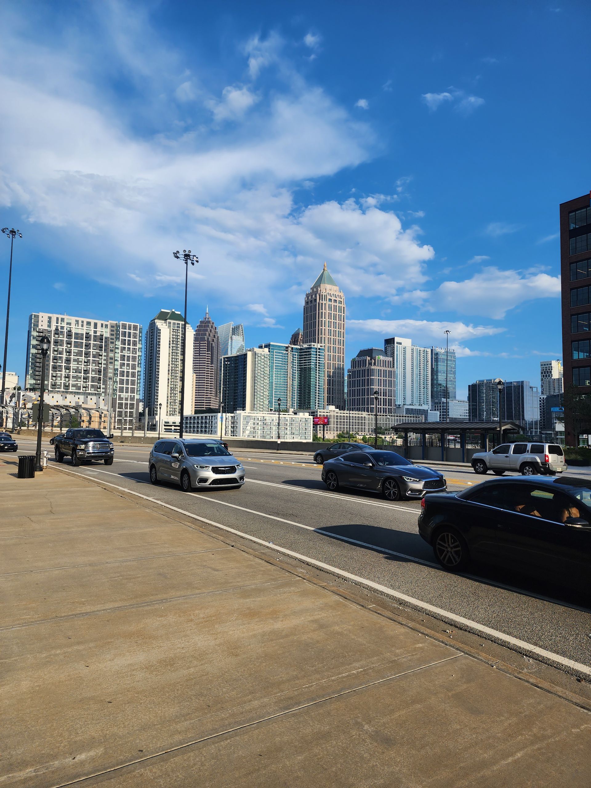 City street with traffic, tall buildings, and a cloudy blue sky.