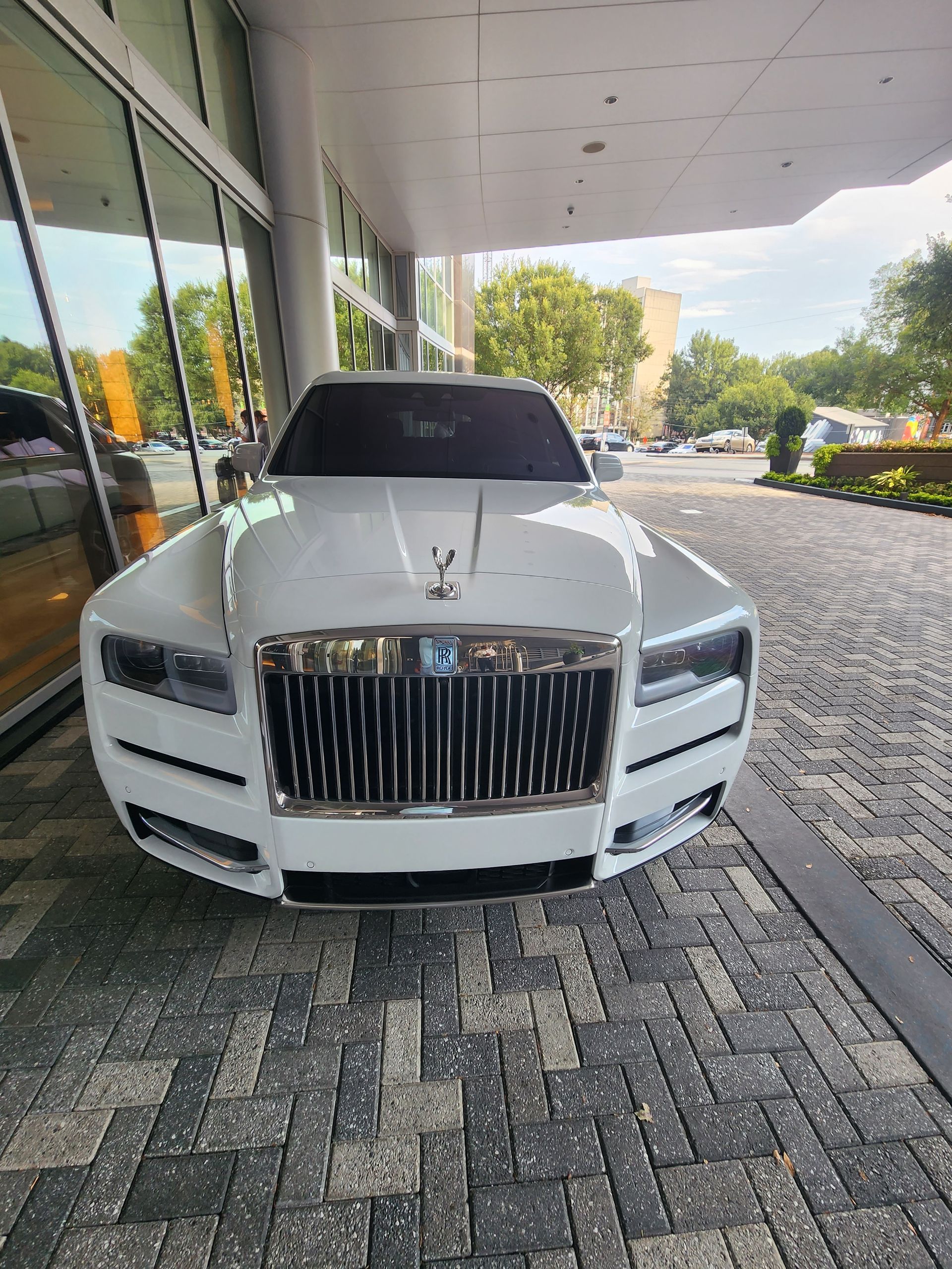 White Rolls-Royce parked under a building overhang with a brick and gray stone floor.