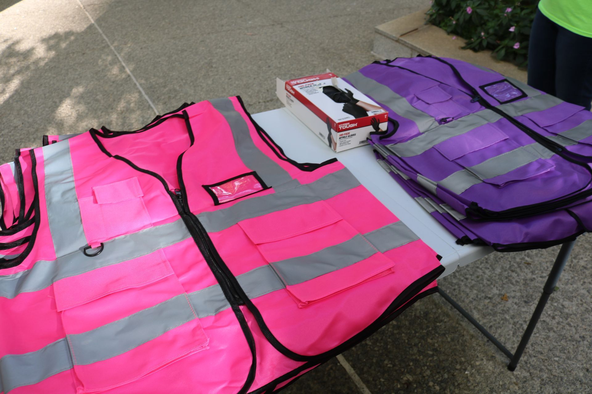 Pink and purple high-visibility vests and a box of black gloves on a white table.