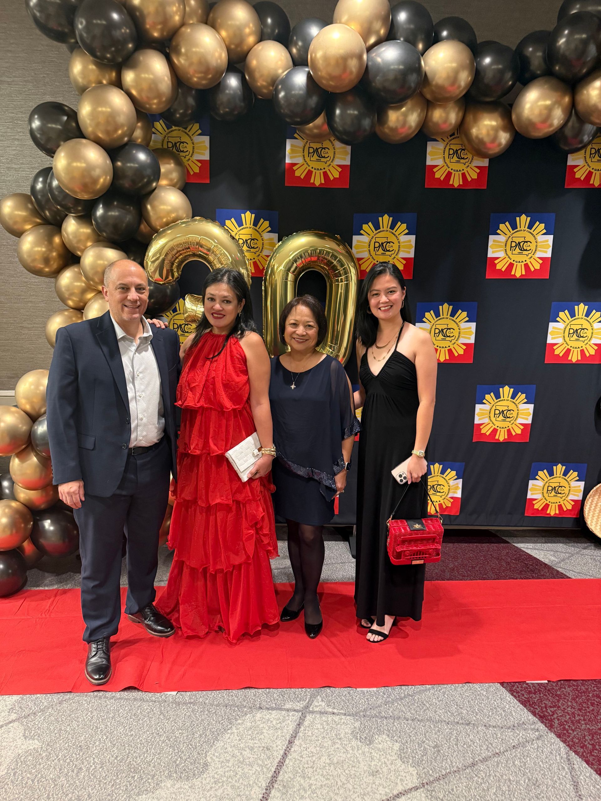 Four people posing on a red carpet in front of a backdrop with balloons and Philippine flags.