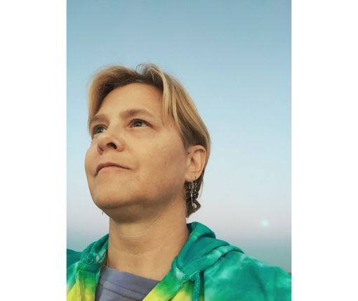 A woman in a tie dye hoodie is looking up at the sky.