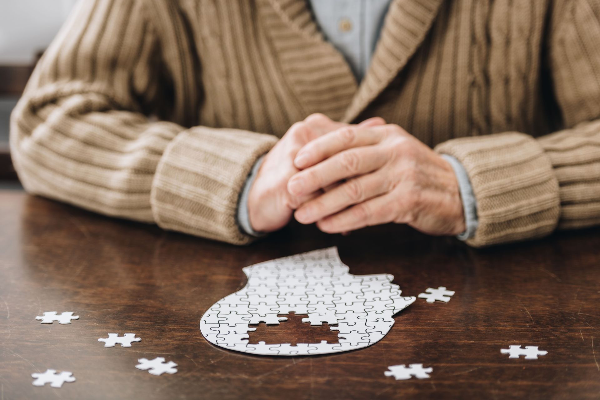 Um homem idoso está sentado à mesa brincando com um quebra-cabeça.