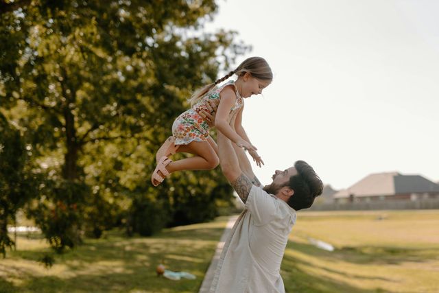 A man is holding a little girl in his arms in the air.