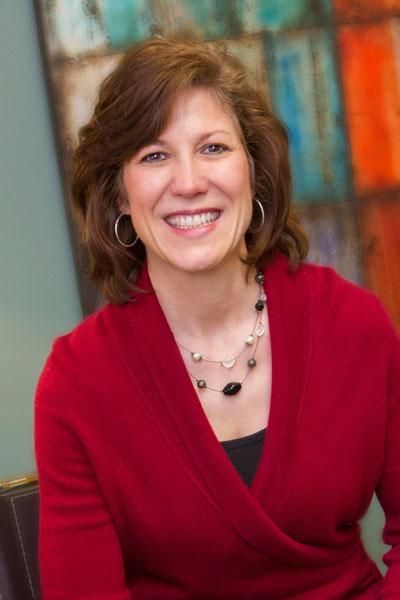 A woman wearing a red sweater and a necklace is smiling for the camera.