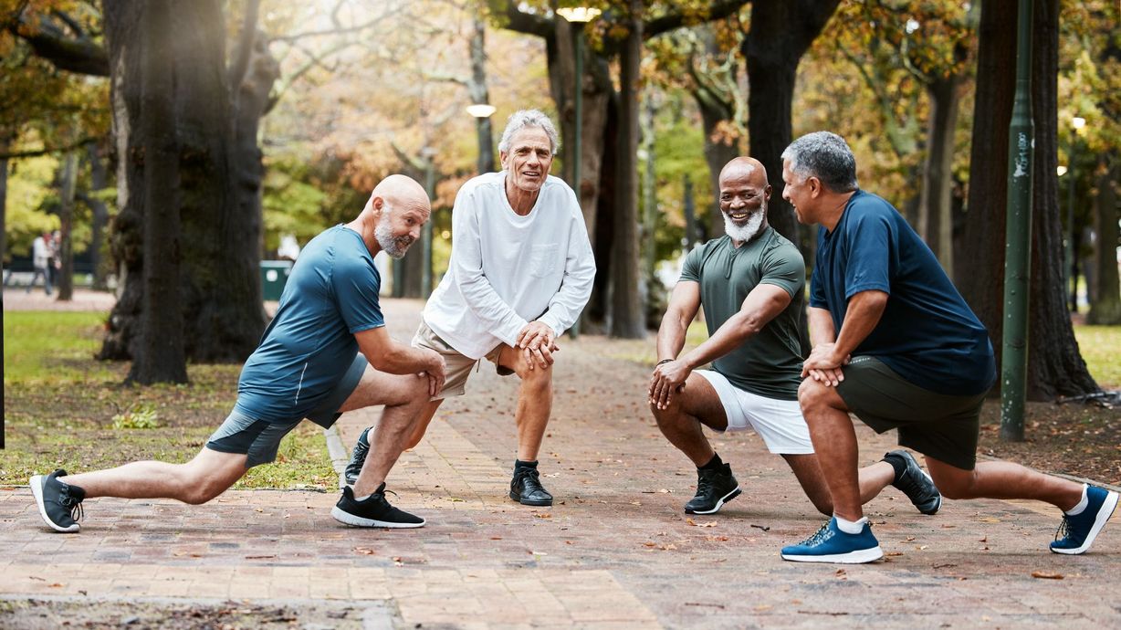 Five older adults doing stretching lunges together in a park