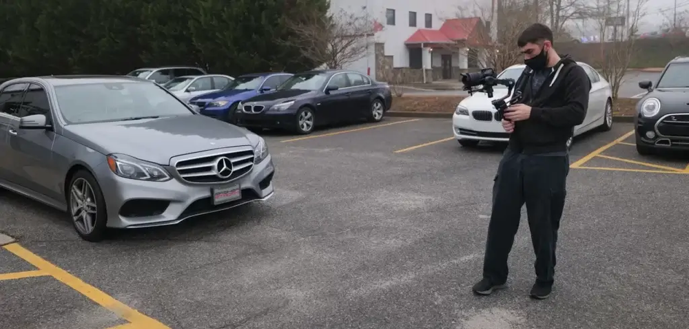 A man is taking a picture of a mercedes in a parking lot.