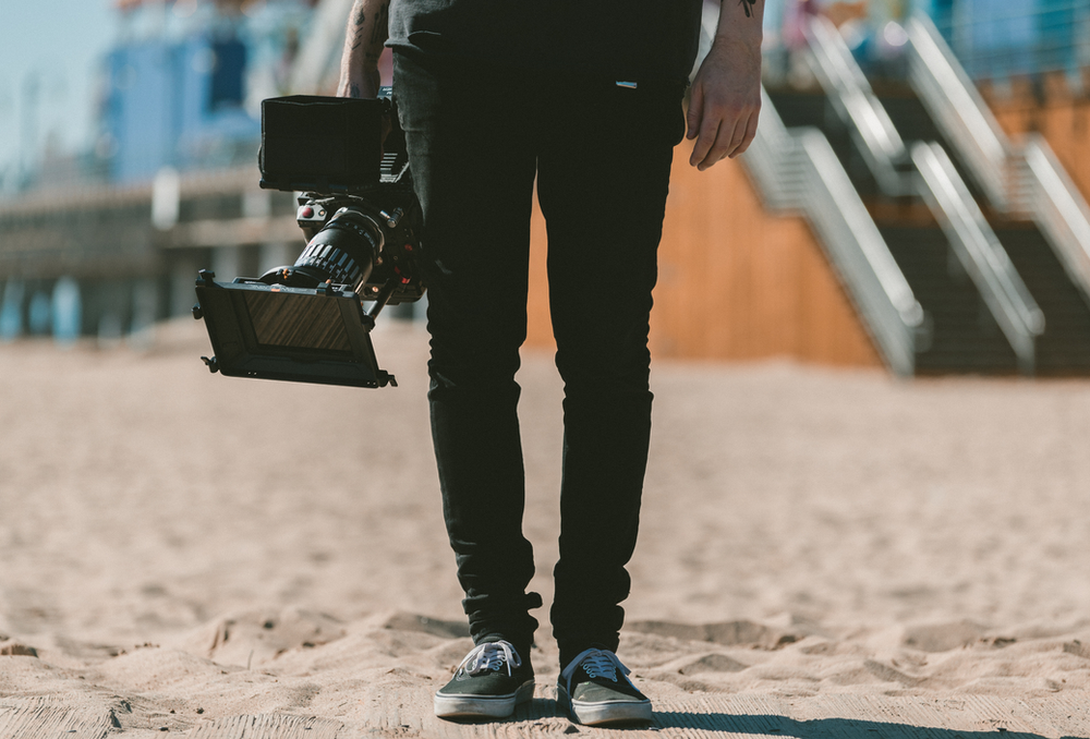 A person is carrying a camera on their shoulder on the beach.