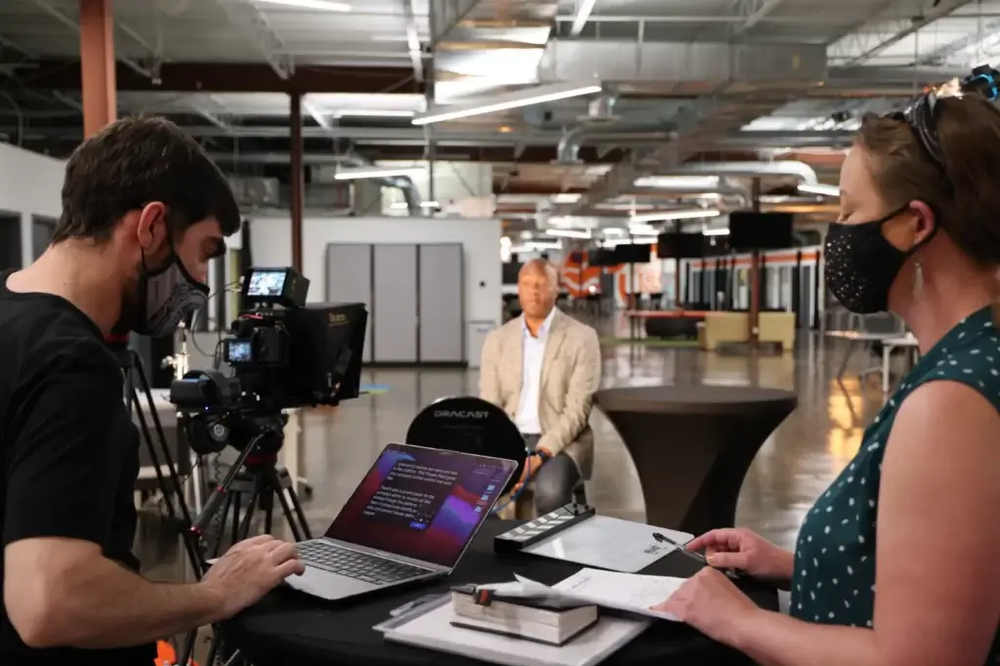 A man and a woman are sitting at a table with a laptop and a camera.