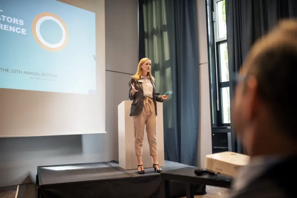 A woman is standing on a stage giving a presentation to a group of people.