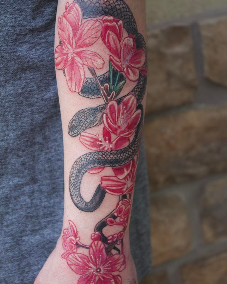 A person has a tattoo of a snake and pink flowers on their arm