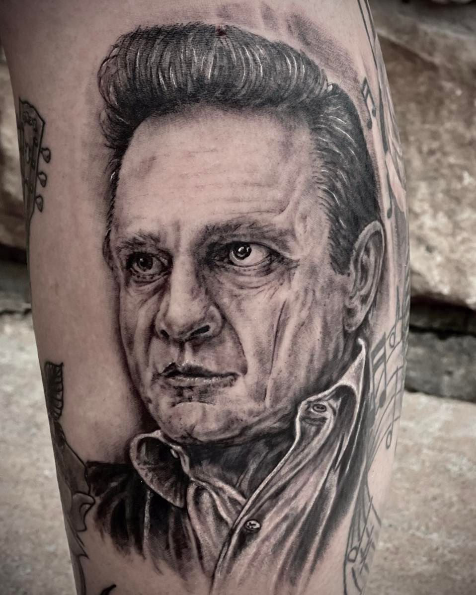 A black and white tattoo of a man 's face on a leg.