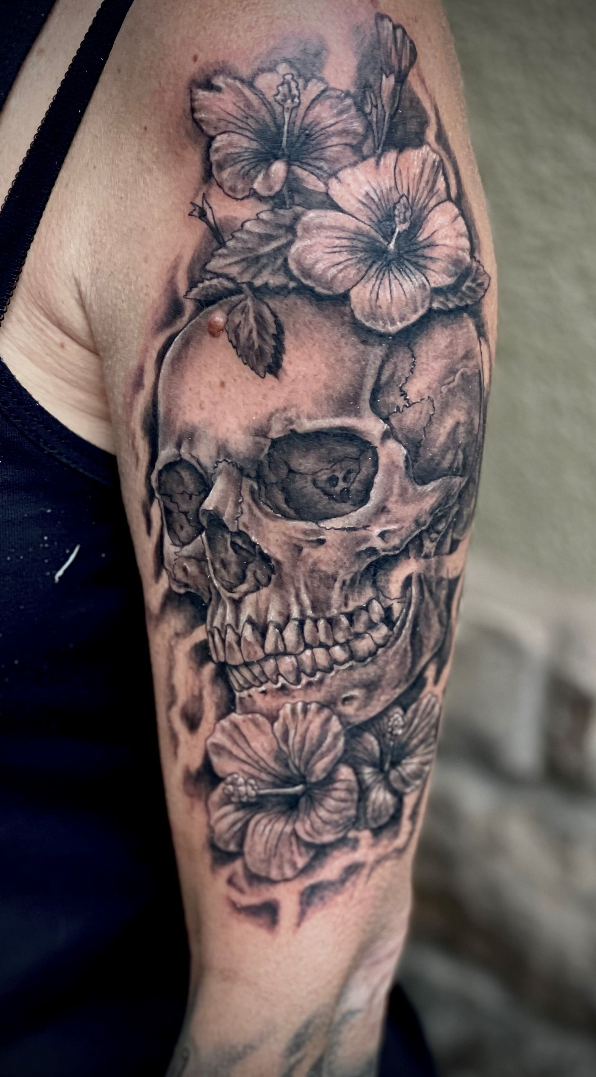 A woman has a tattoo of a skull with flowers on her arm.