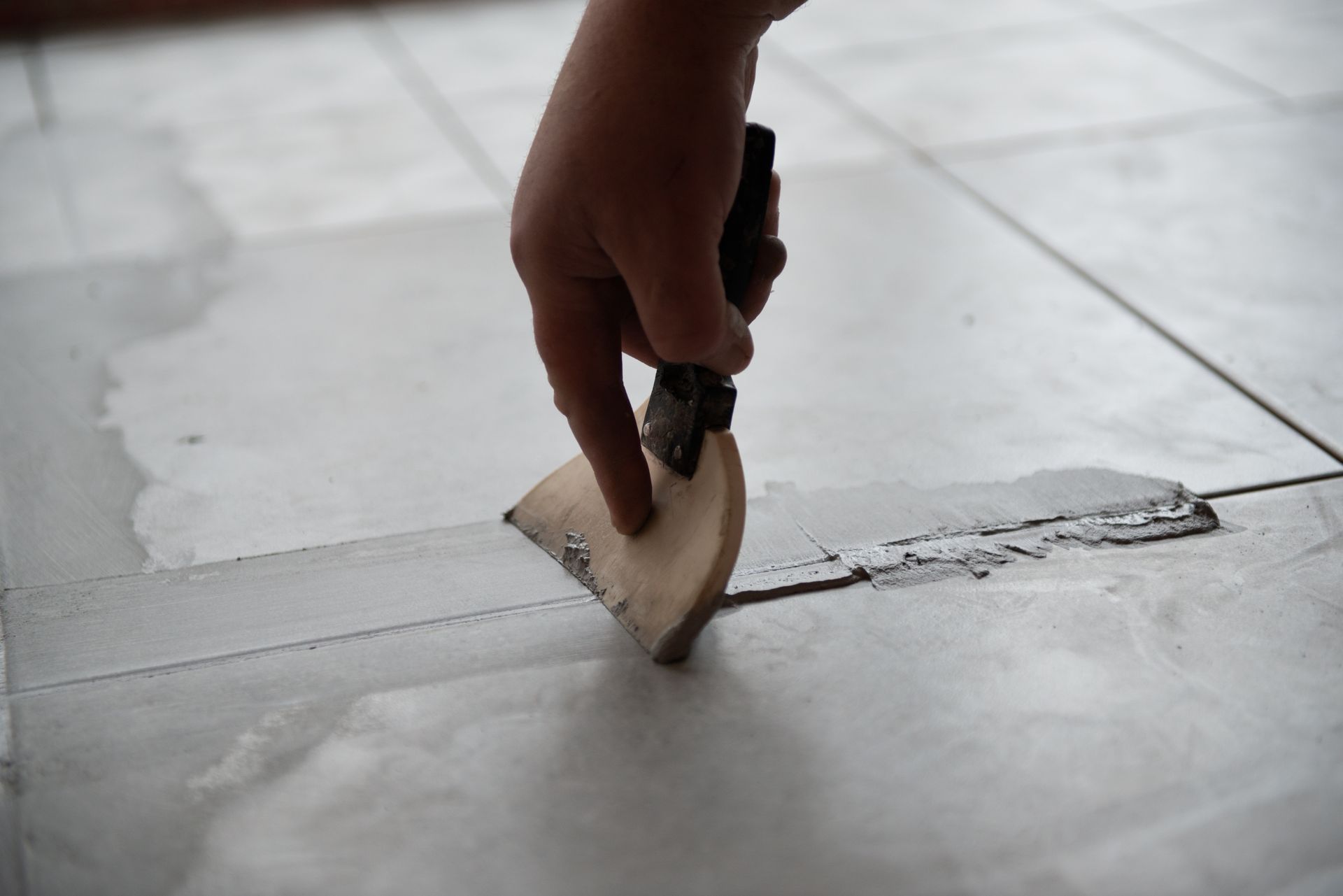 A person is plastering a tile floor with a spatula.