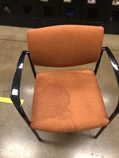 An orange chair with black armrests is sitting on a concrete floor.