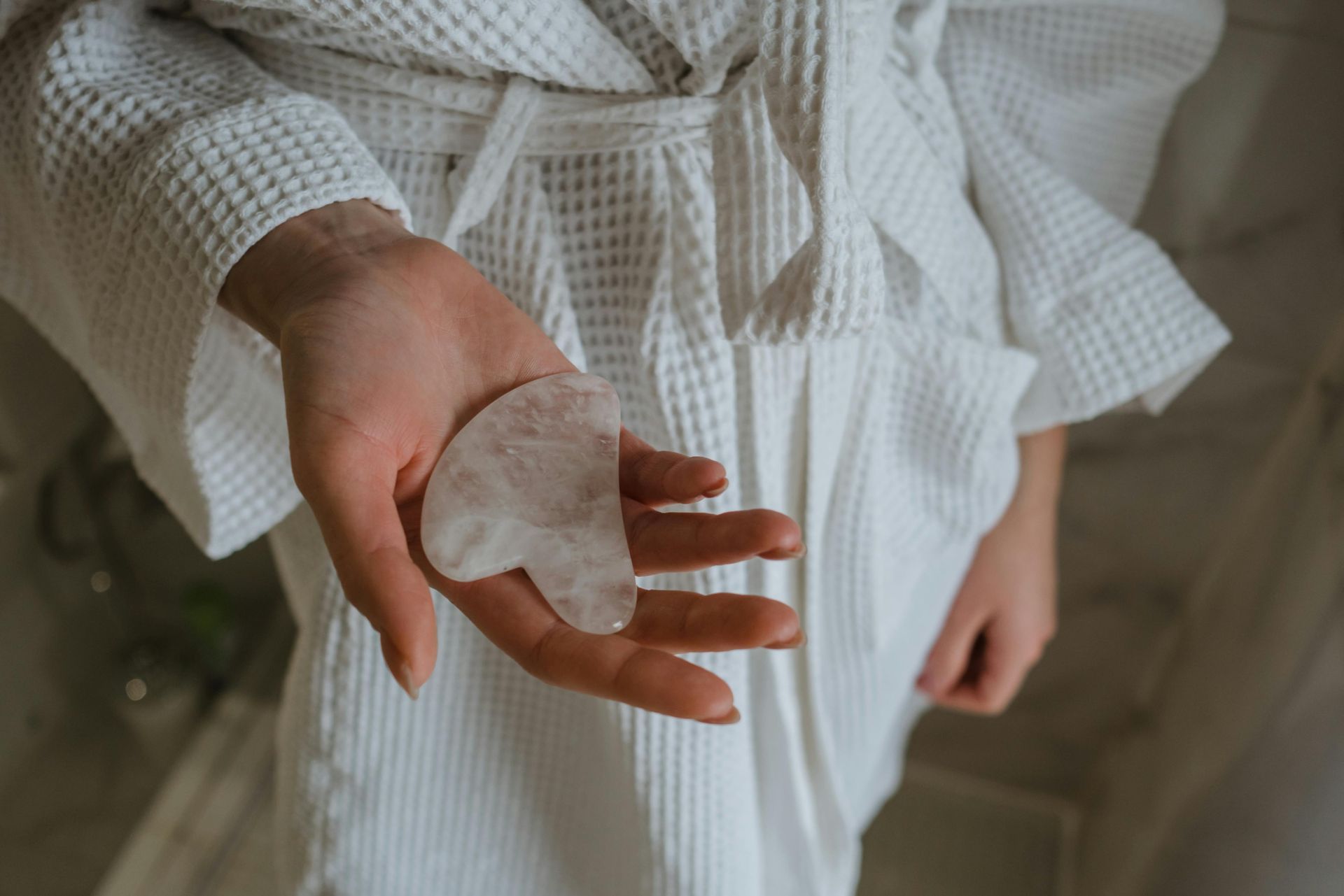A woman in a white robe is holding a gua sha in her hand.