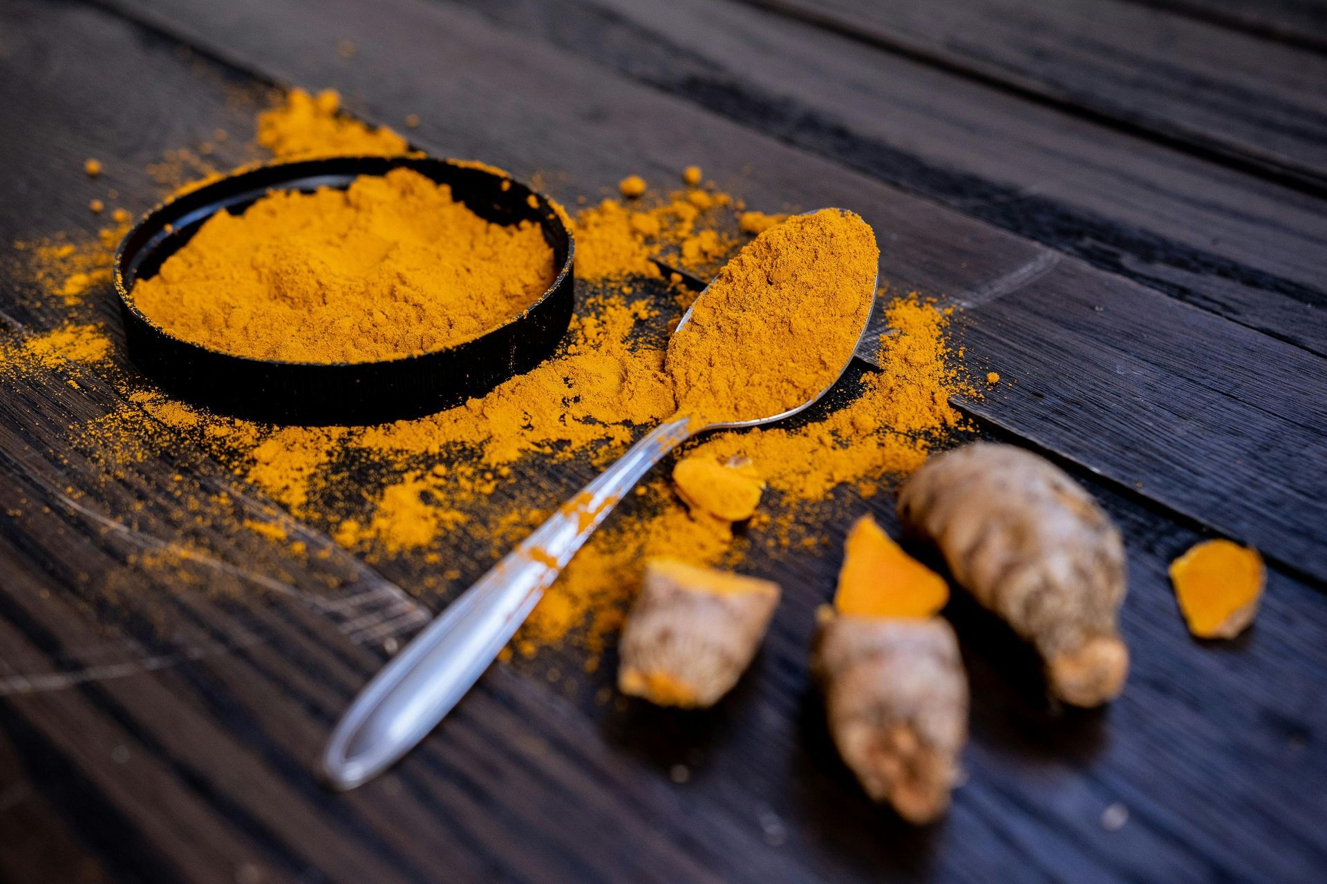 A bowl of turmeric powder and a spoon on a wooden table.