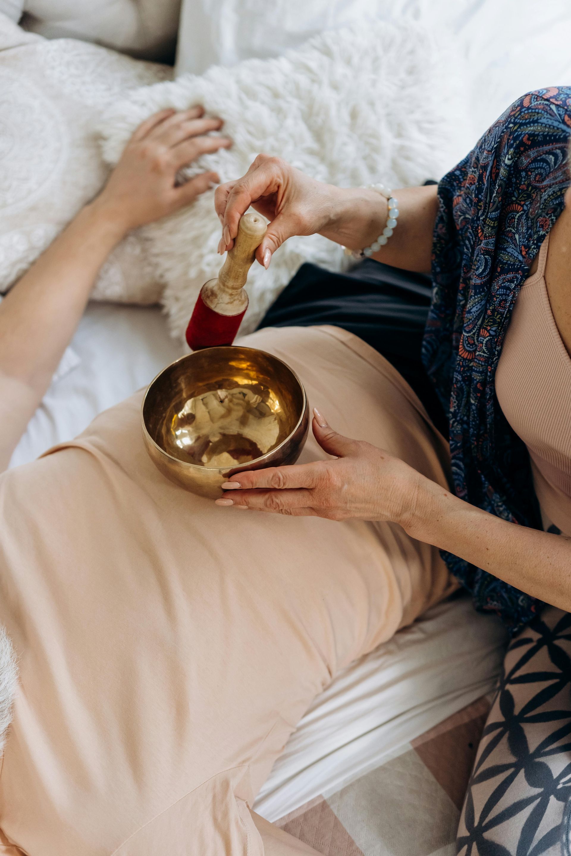 A woman is sitting on a bed holding a singing bowl.