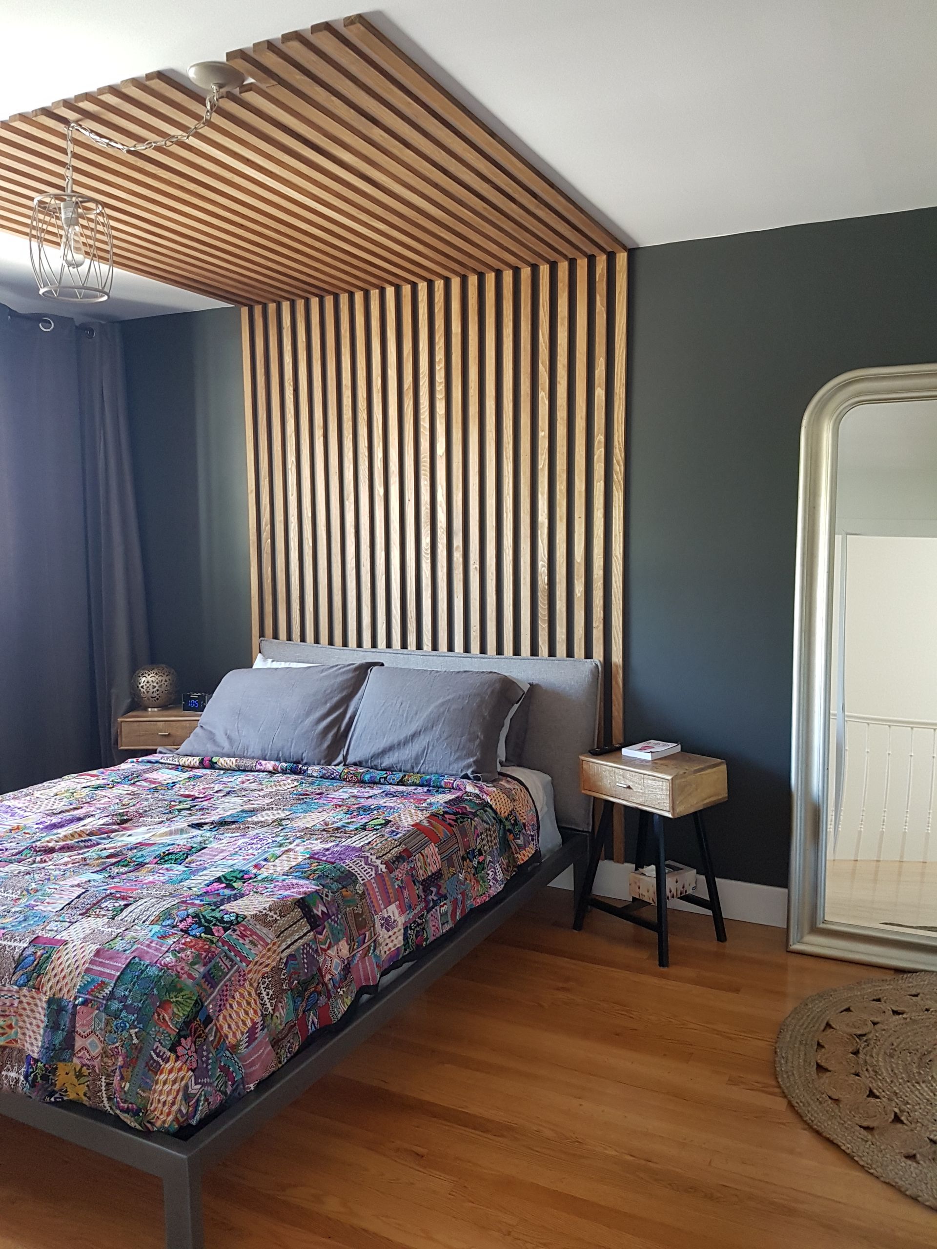 Une chambre avec un lit, une table de nuit, un miroir et une tête de lit en bois.