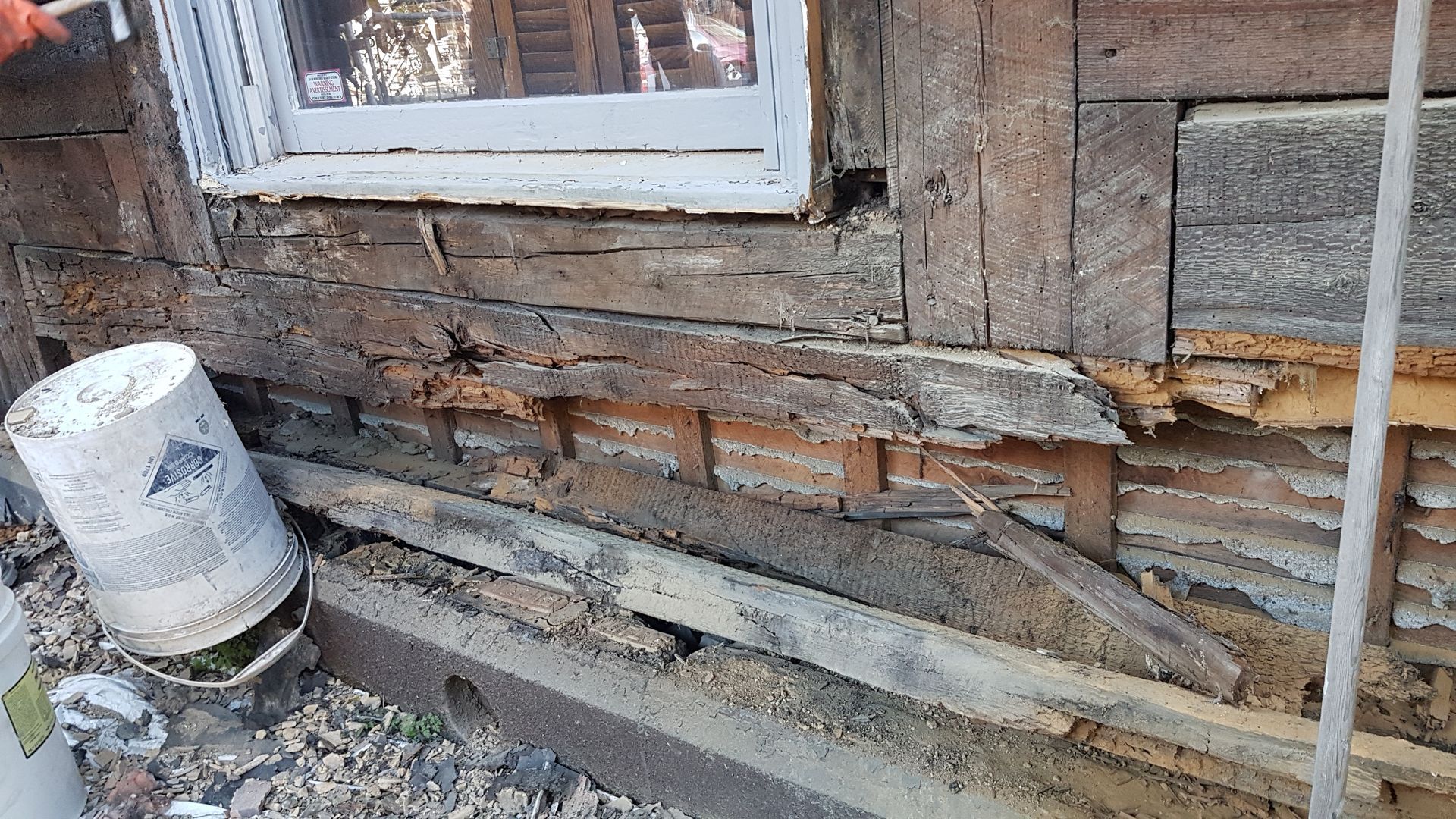 Un mur en bois avec une fenêtre et un seau à côté.
