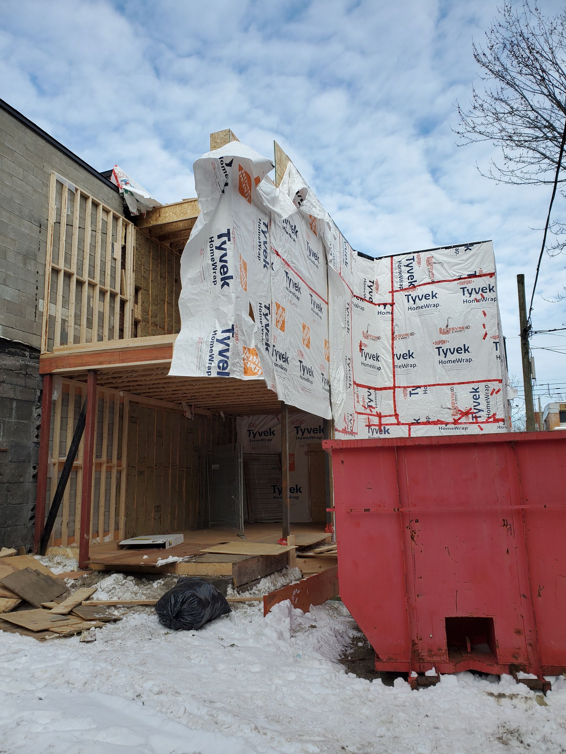 Un bâtiment est en construction dans la neige à côté d'une benne rouge.