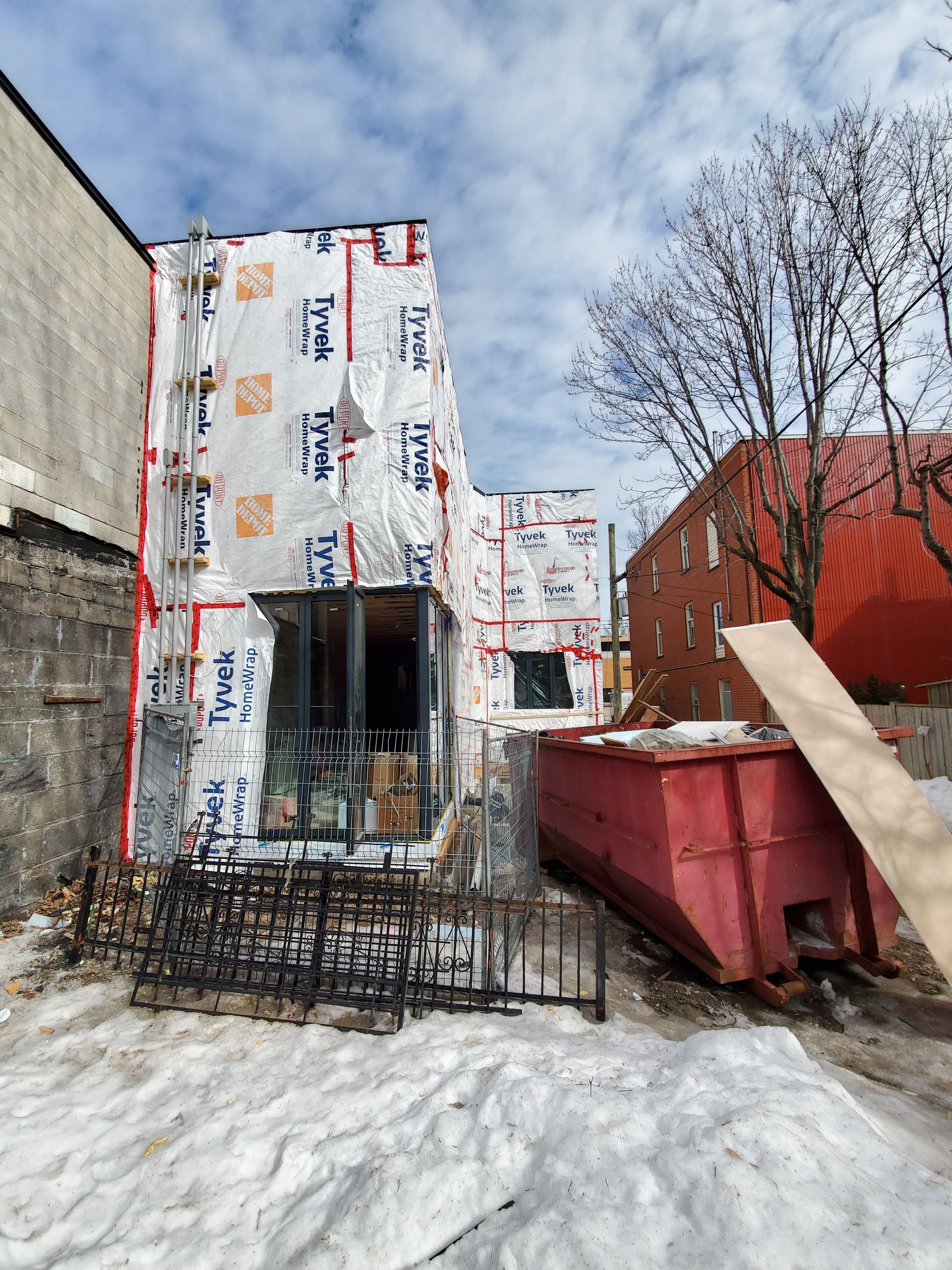 Une benne rouge se trouve devant un bâtiment en construction.