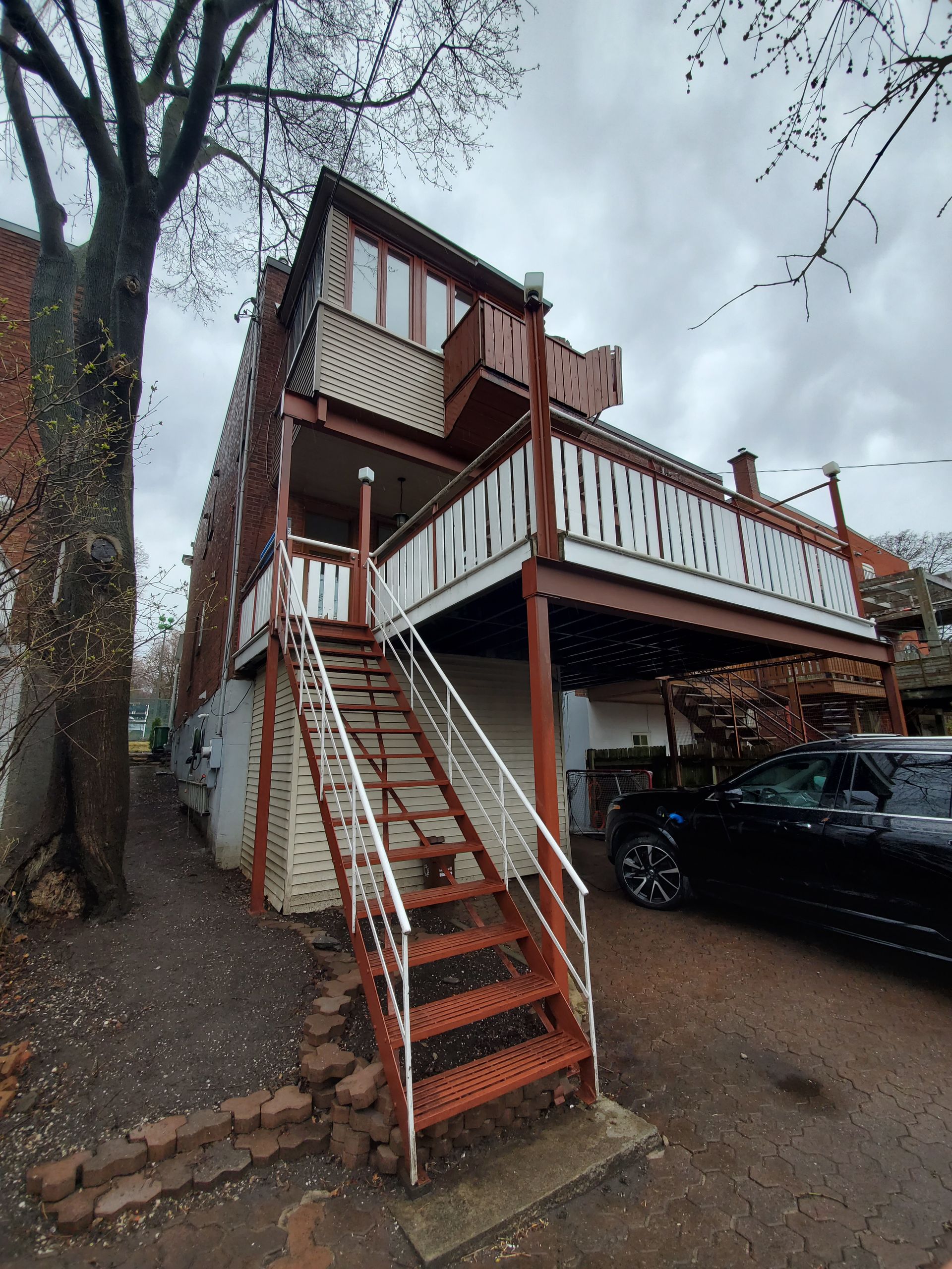 Une maison avec des escaliers menant au deuxième étage et une voiture garée devant.