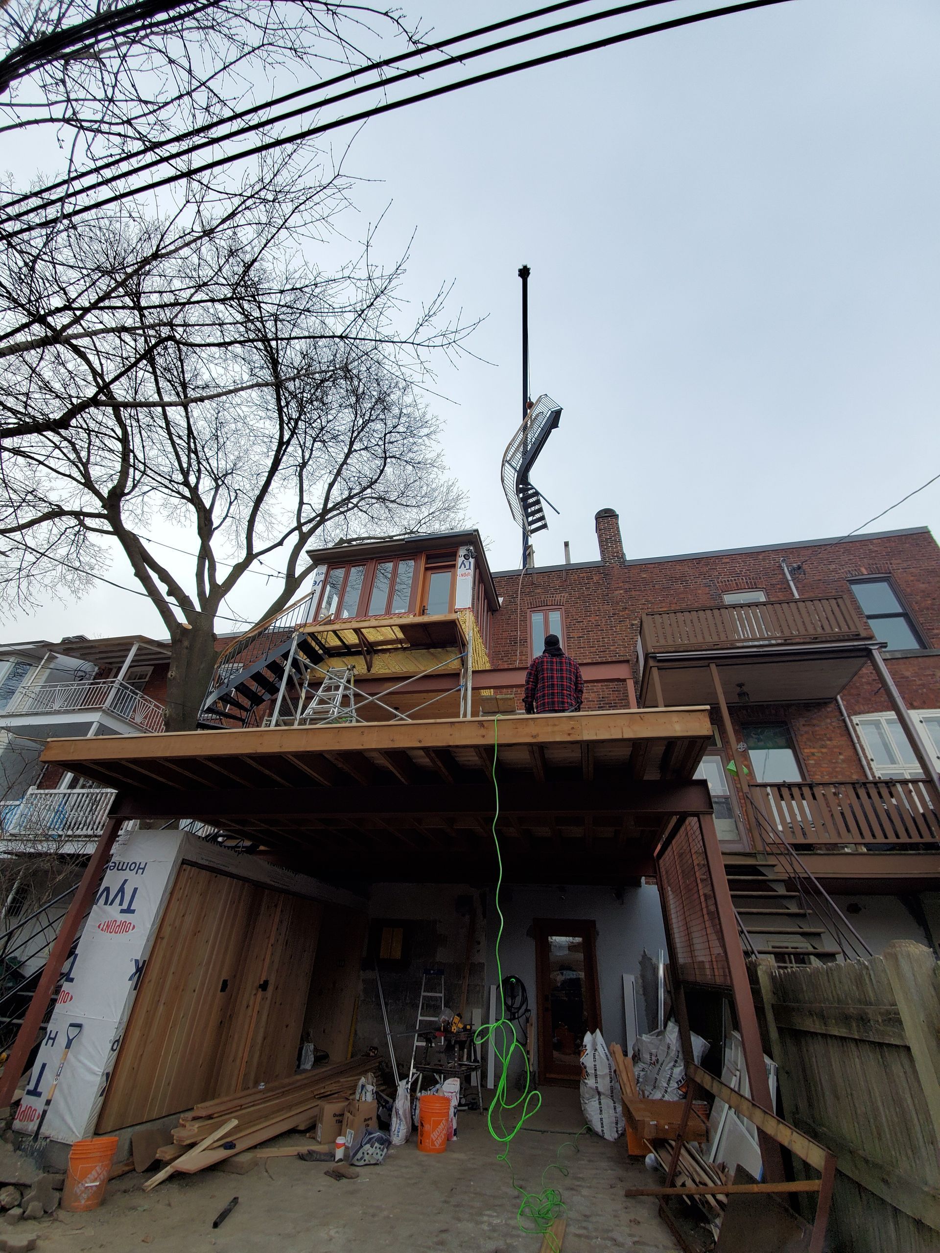 Un homme se tient au sommet d'une terrasse en bois devant un bâtiment en brique.