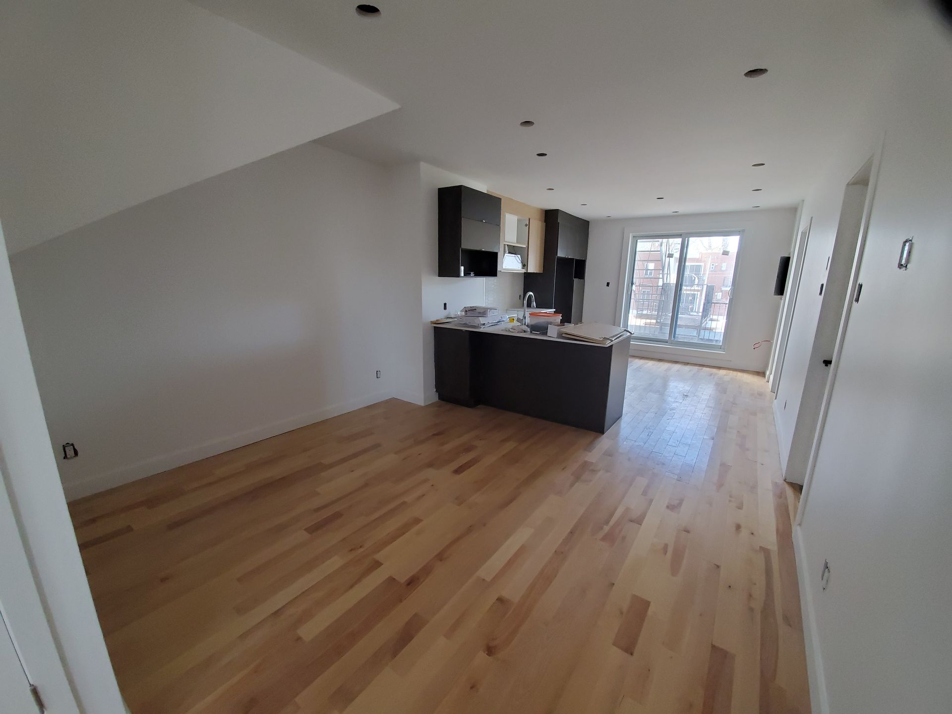 Un salon avec parquet et une cuisine en arrière-plan