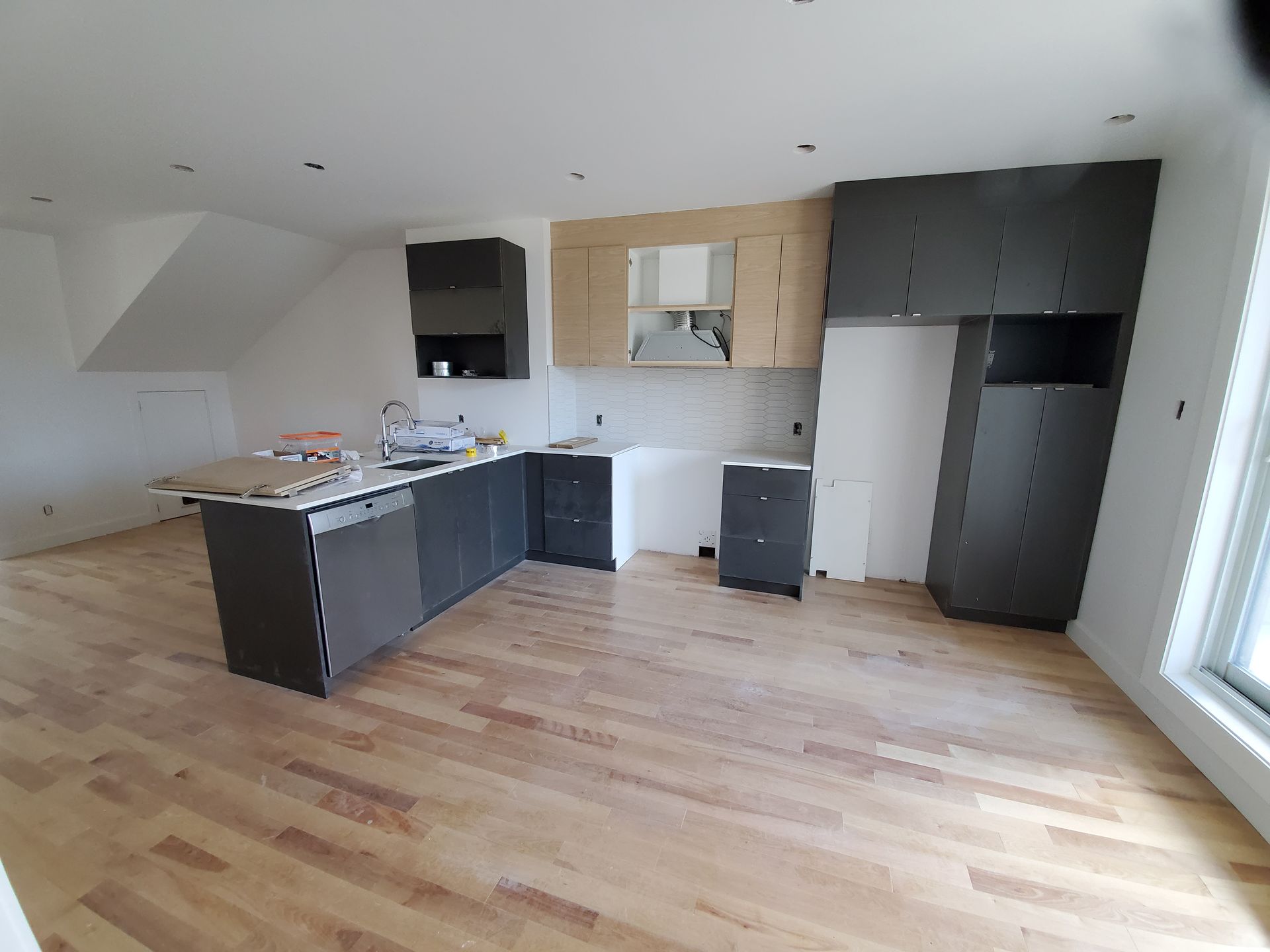 Une cuisine avec parquet et armoires noires est en cours de rénovation.