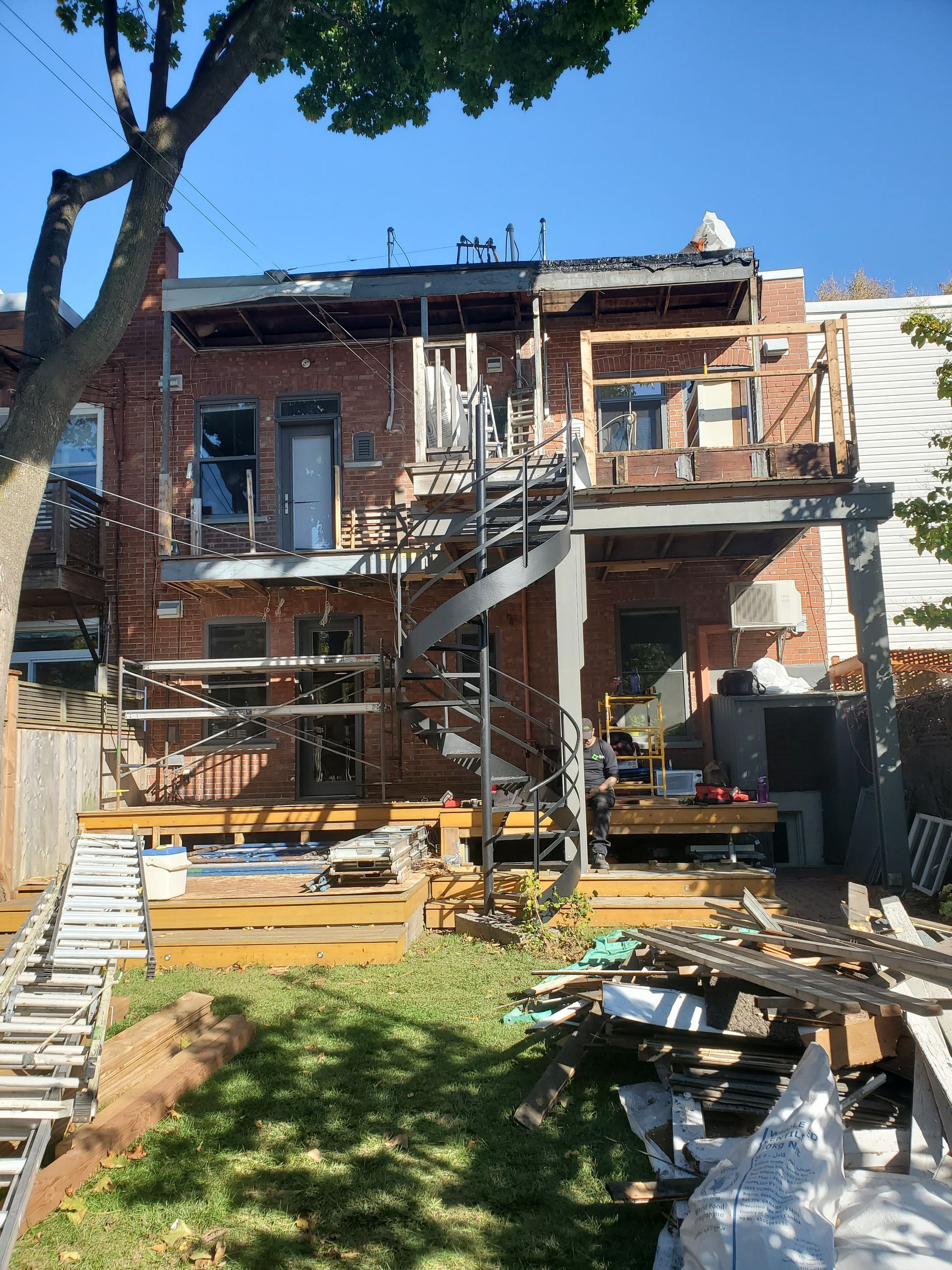 Une maison en brique est en cours de rénovation avec une terrasse et des escaliers en bois.