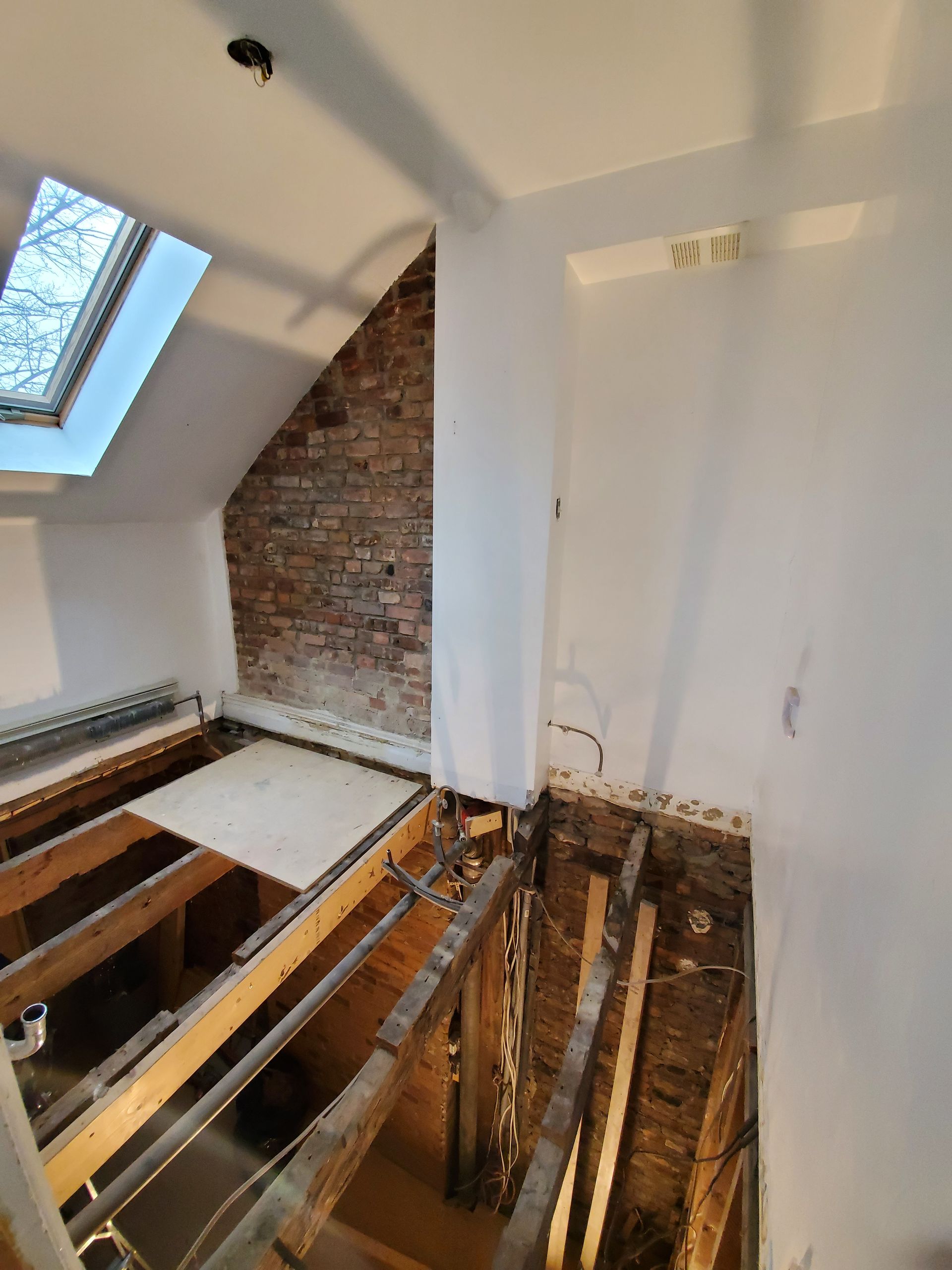 Une pièce avec un mur de briques et une lucarne au plafond.