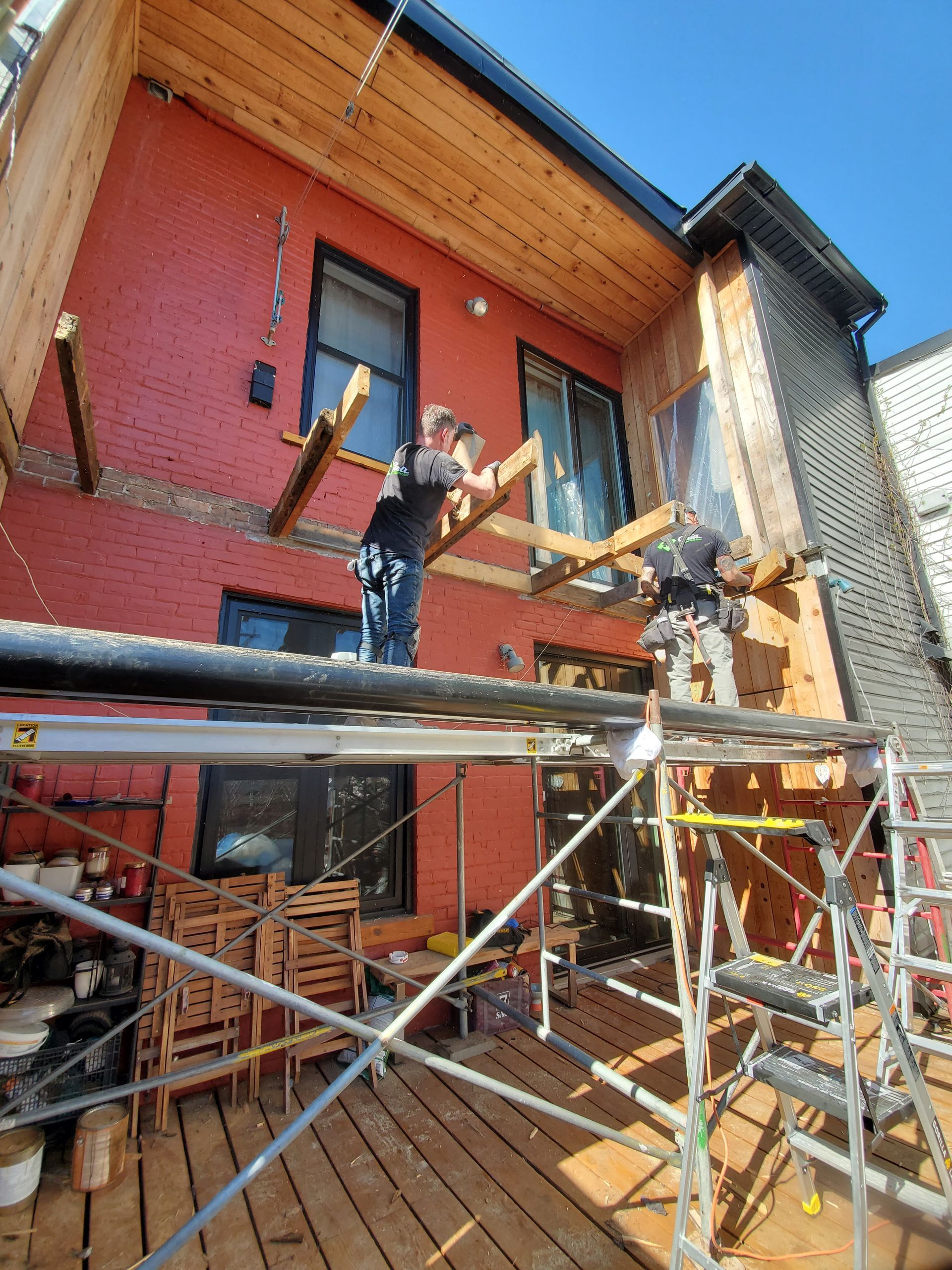 Un homme est debout sur un échafaudage devant une maison rouge.