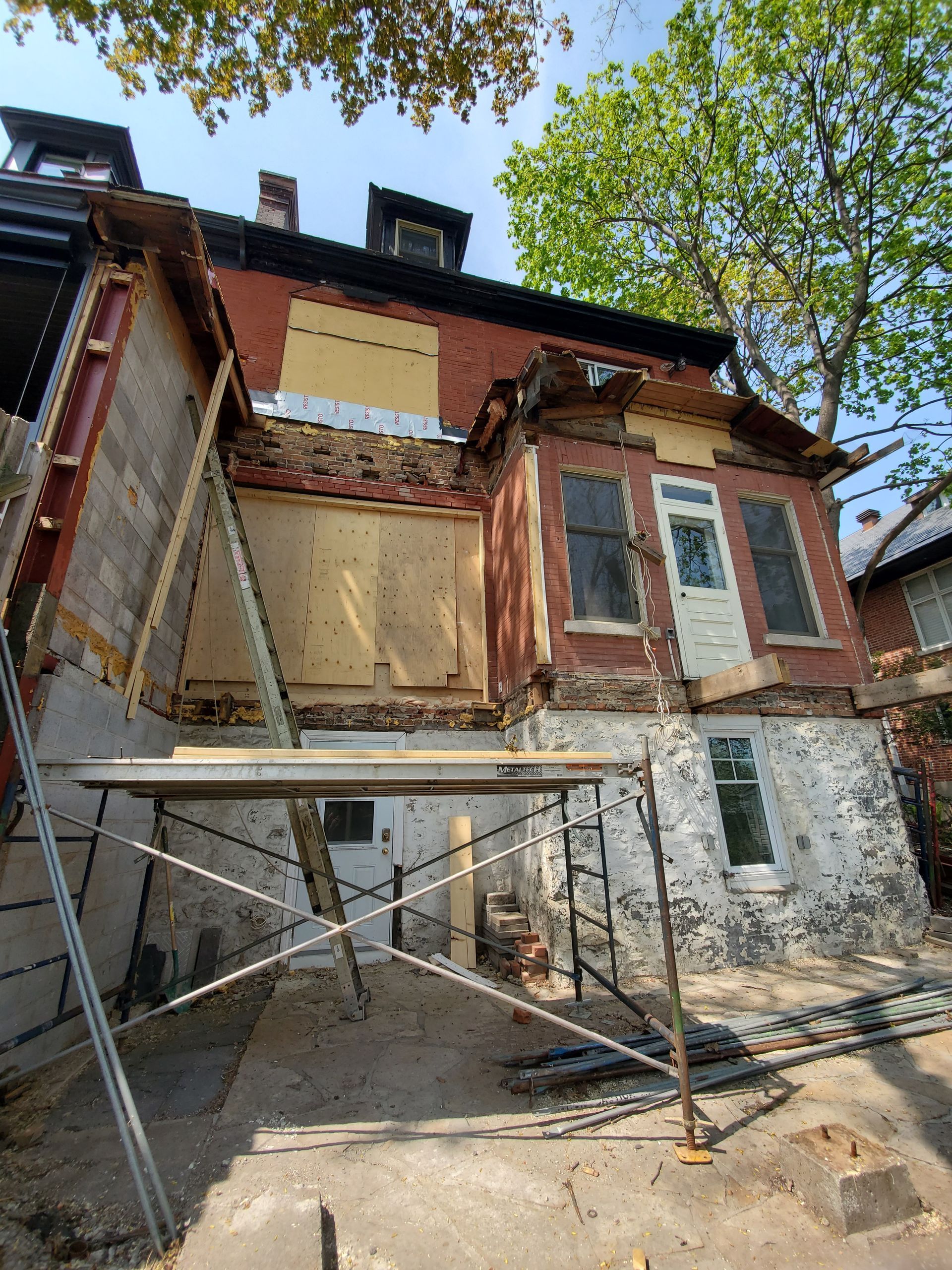 Une maison en briques est en train d'être démolie et un échafaudage se trouve devant.