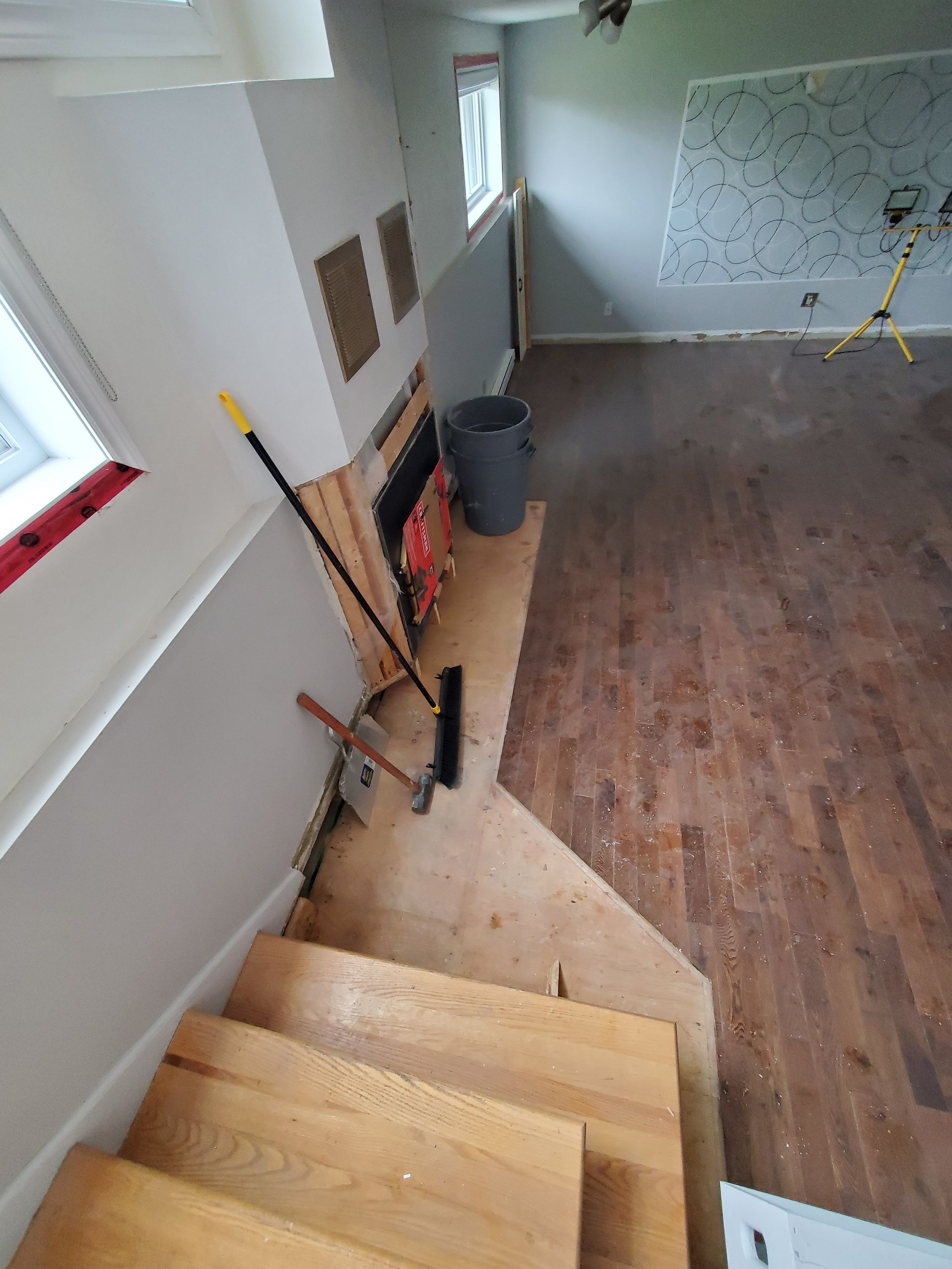 Une pièce avec un escalier en bois et un balai au sol.