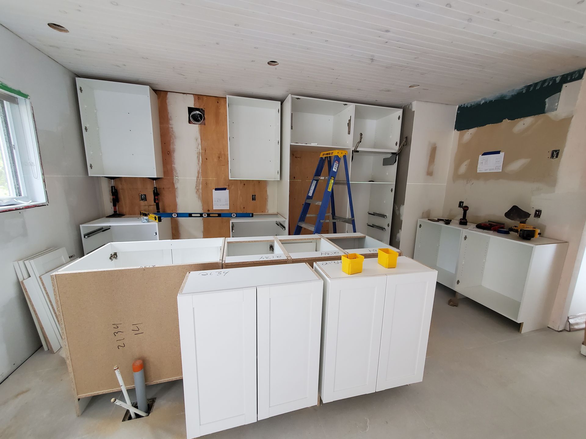 Une cuisine en construction avec des armoires blanches et une échelle bleue.