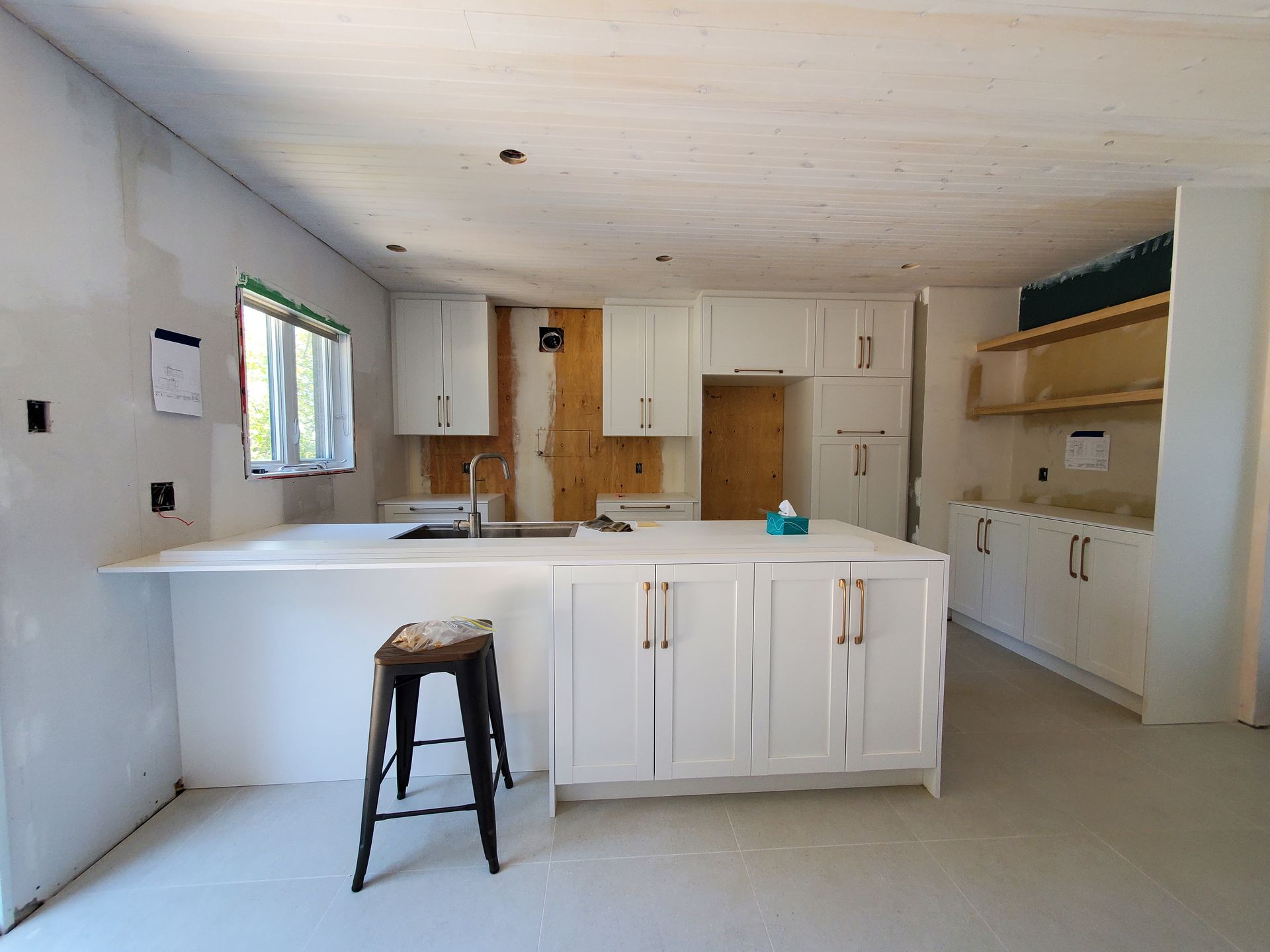 Une cuisine en construction avec des armoires blanches et un tabouret